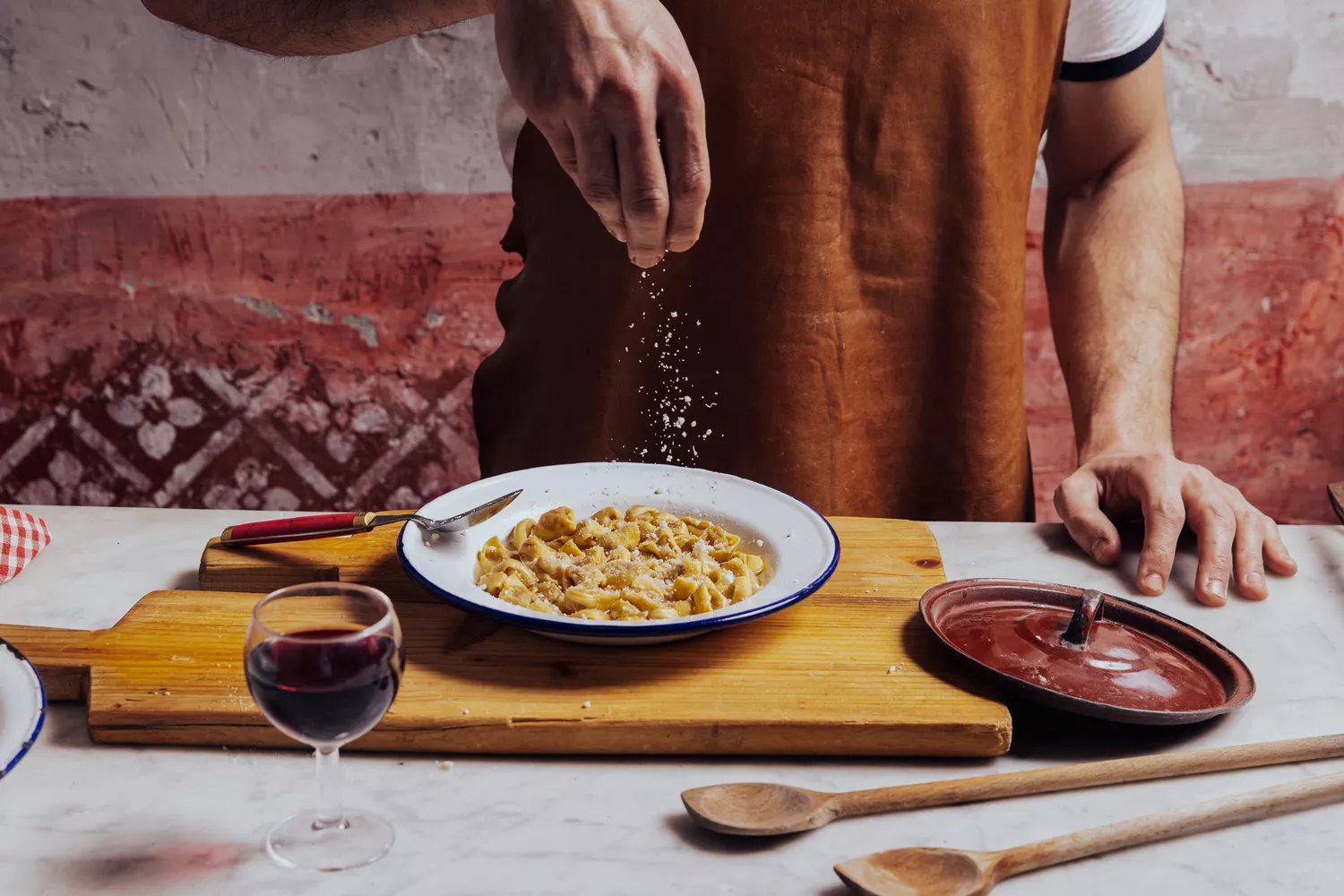 Close-up of a chef sprinkling parmesan cheese on a plate of fresh tortellini.