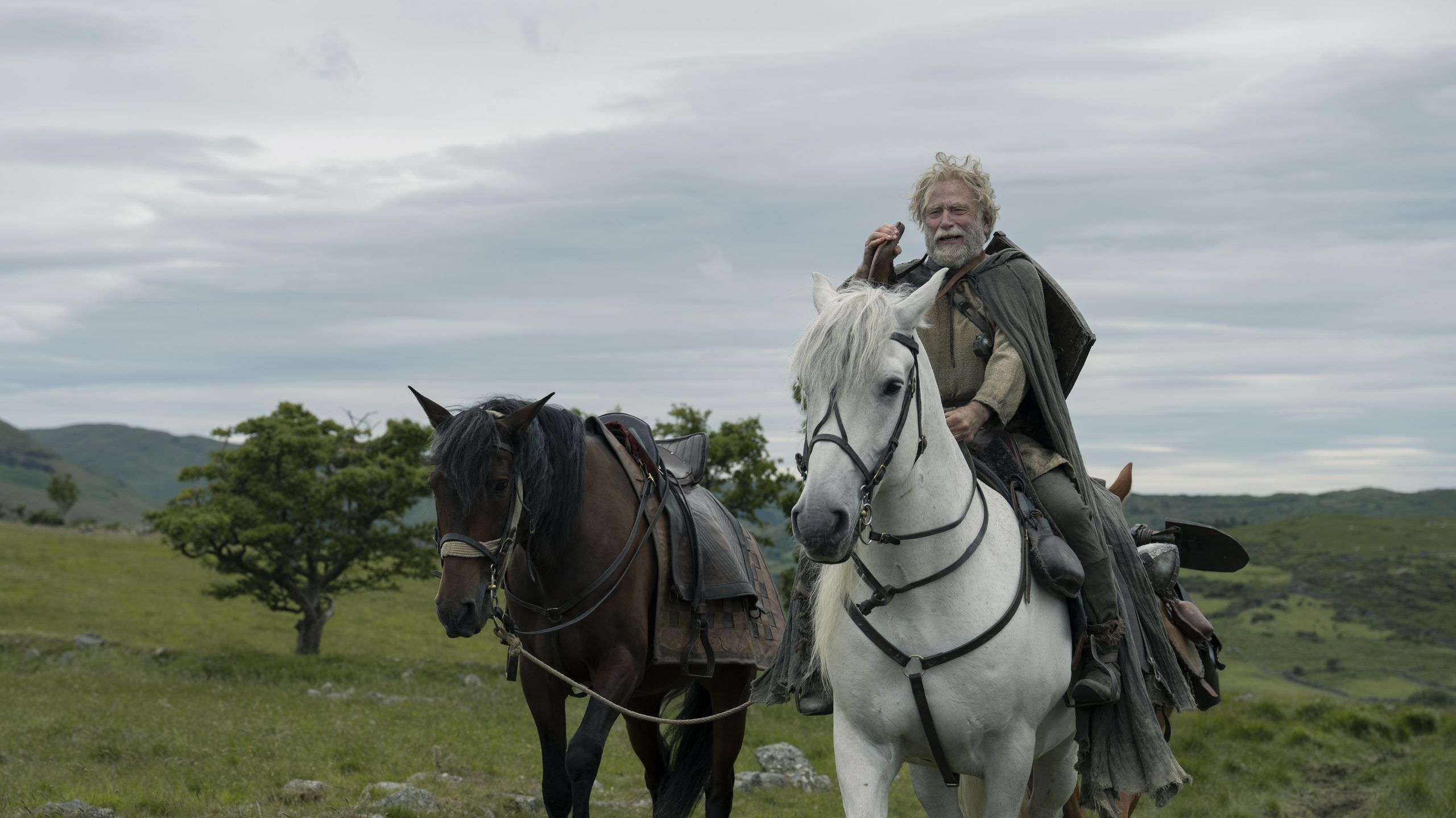 Actor Danny Webb in medieval costume riding a horse through a field.
