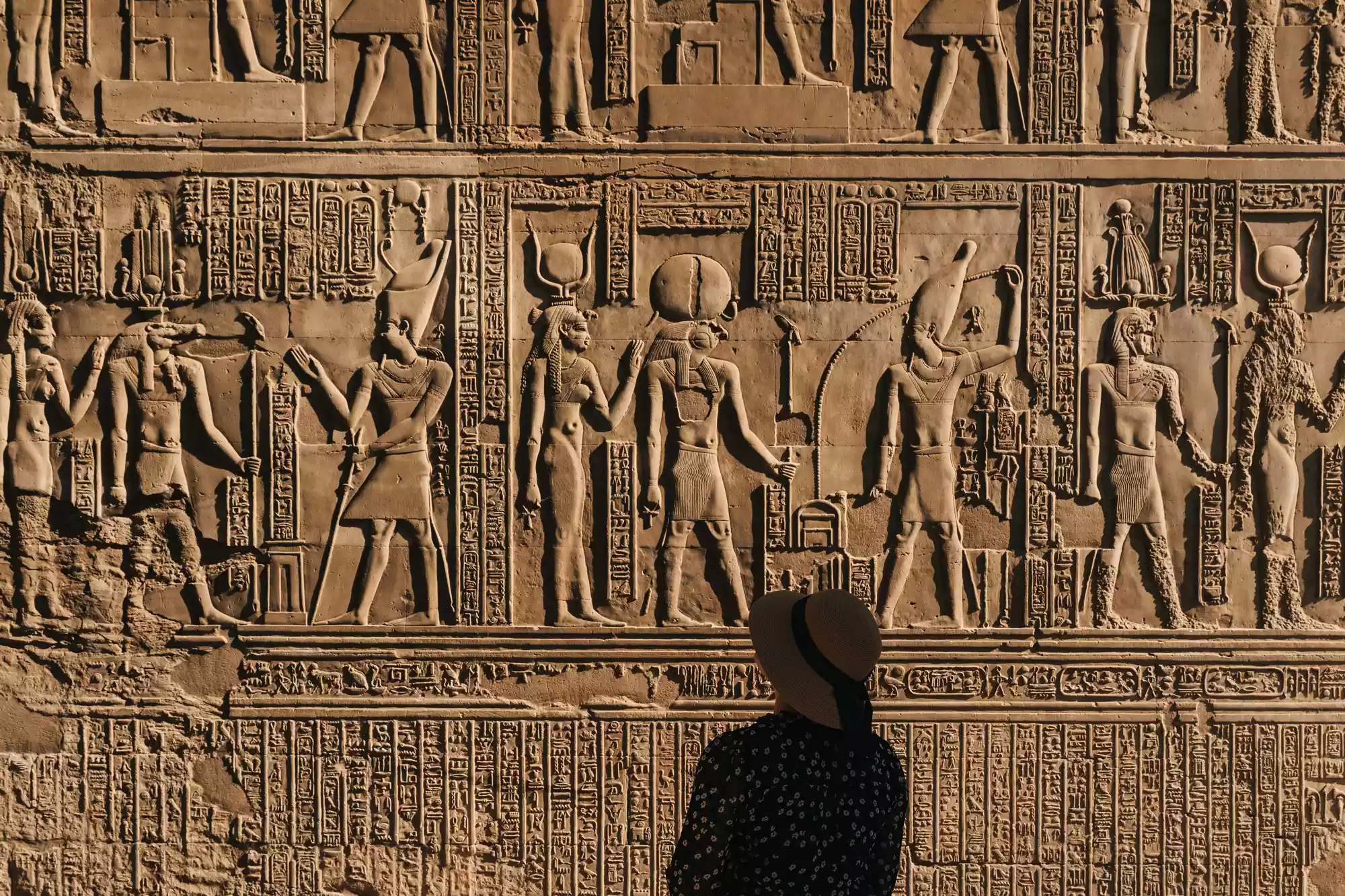 Silhouette of a traveler observing ancient Egyptian hieroglyphics in a stone temple.
