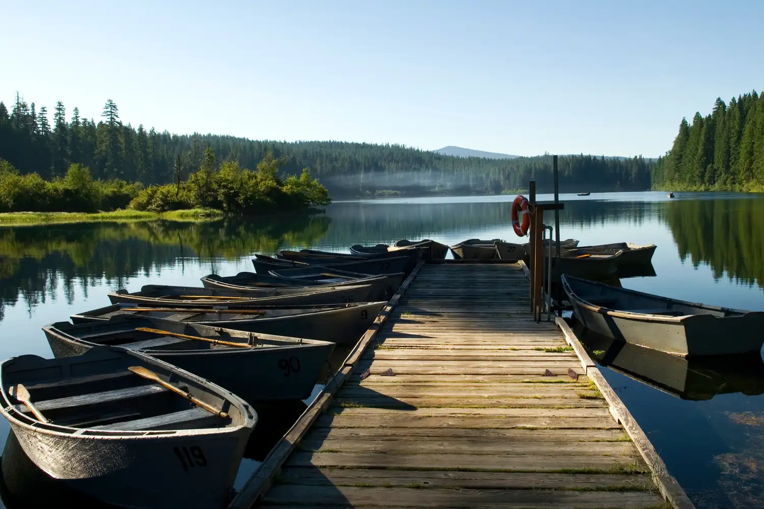 Wooden dock and canoes on a tranquil lake in Central Oregon surrounded by lush greenery.
