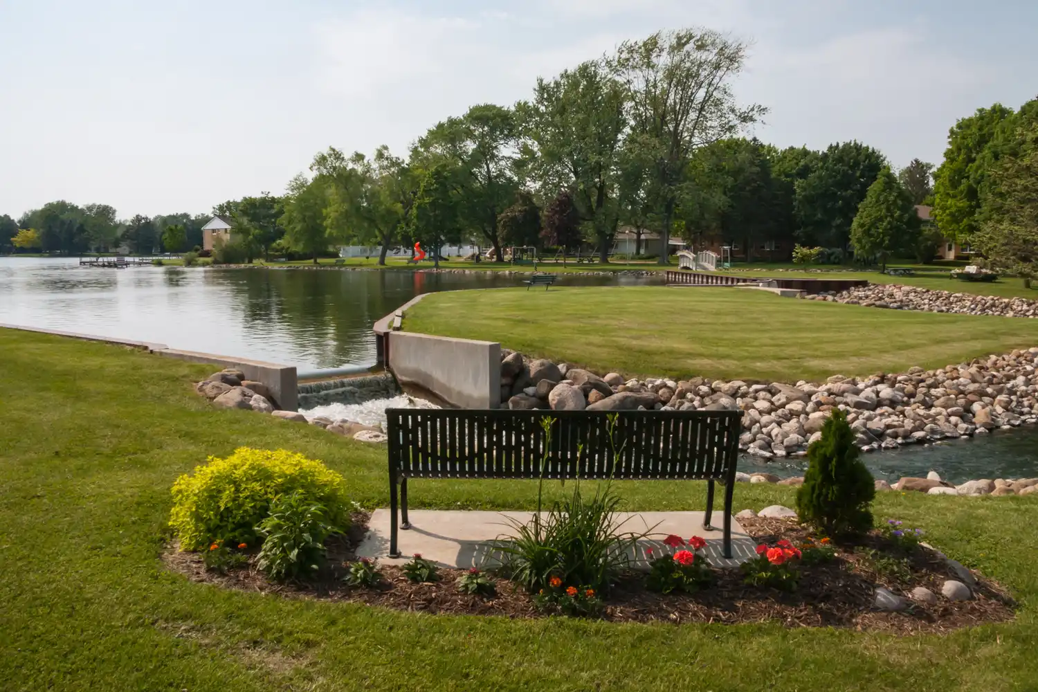 A peaceful park scene at Green Lake, Wisconsin, with a wooden bench overlooking calm water and manicured landscaping.