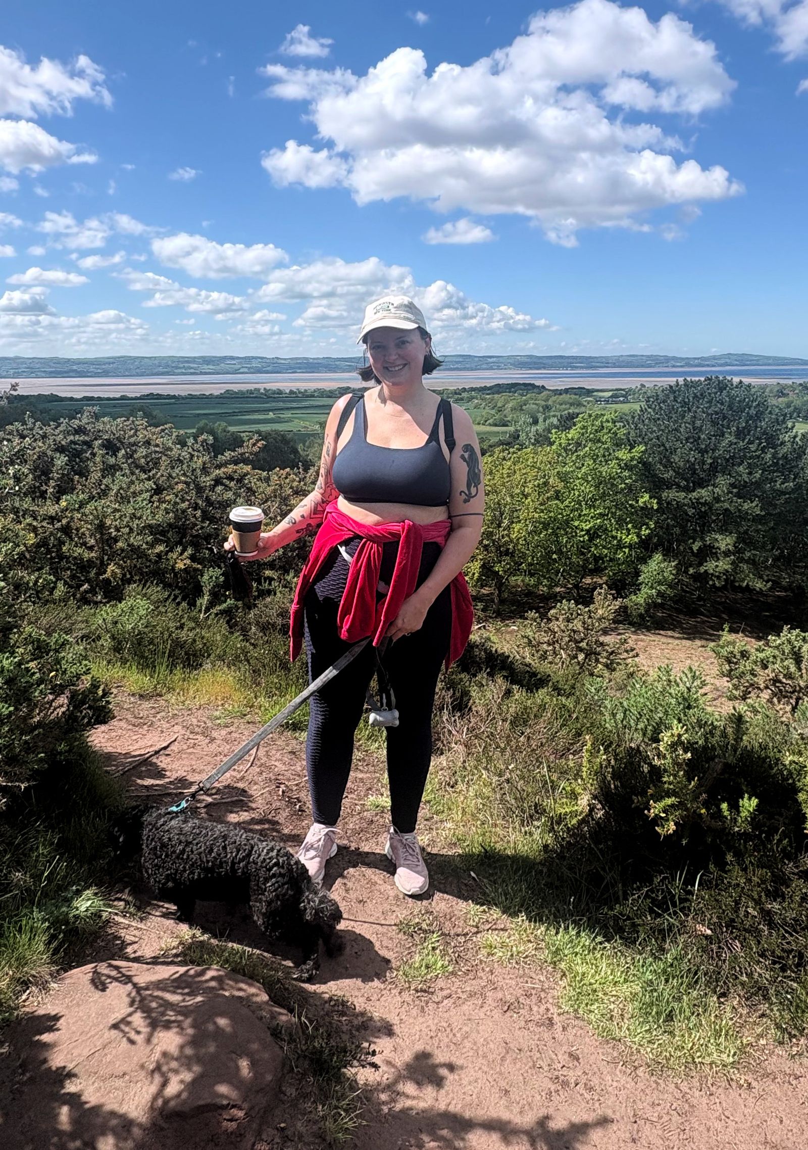A hiker smiling with a dog on a scenic outdoors path.