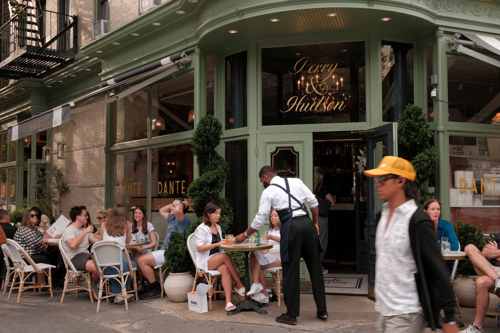 The sidewalk cafe at Dante West Village featuring woven chairs and small round tables.