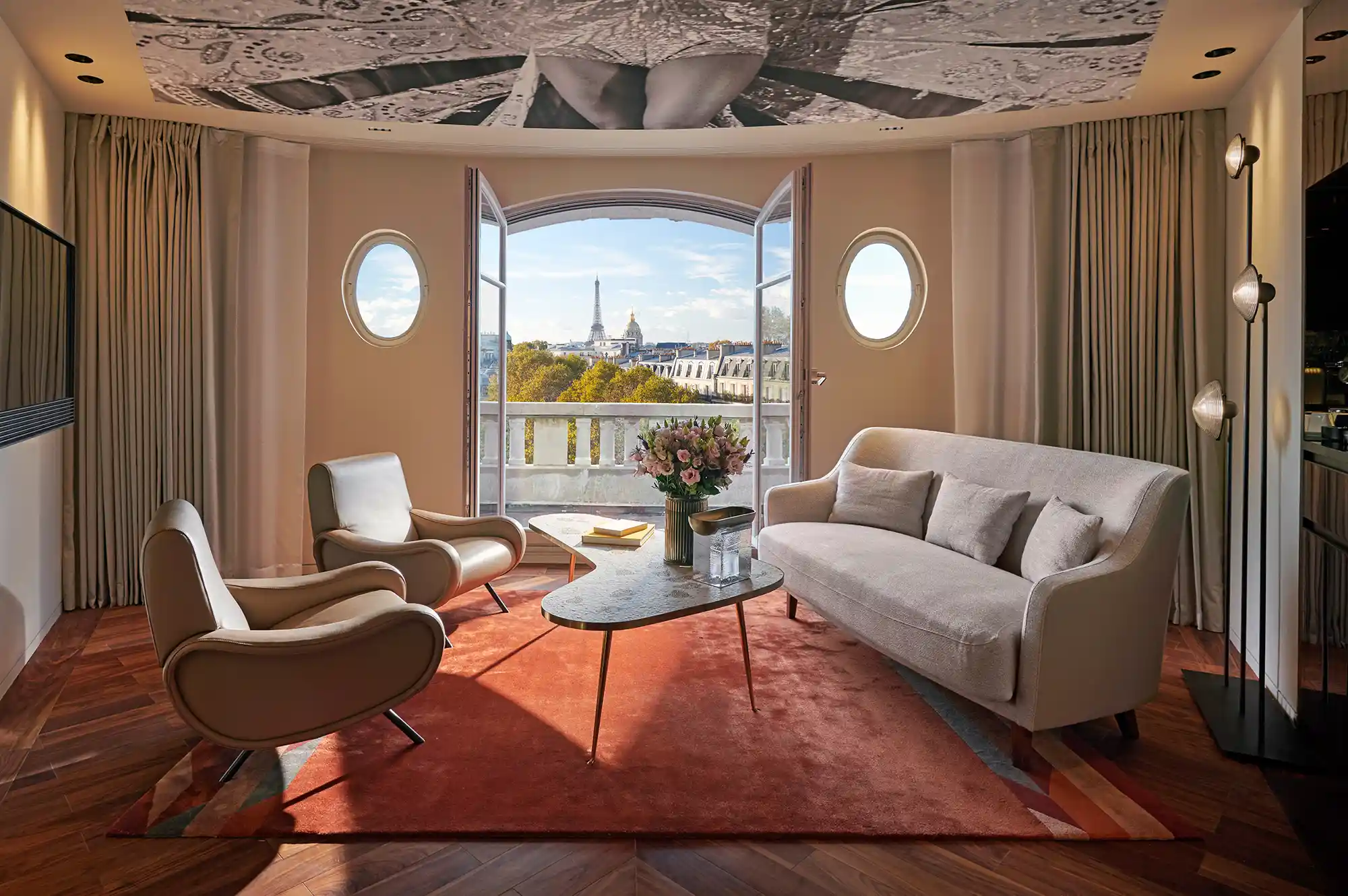 A luxury hotel suite living room with wooden floors and a large window framing the Eiffel Tower.