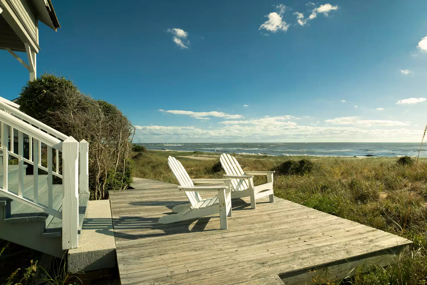 Coastal cottage exterior with a boardwalk and chairs overlooking the sand dunes and Atlantic Ocean.