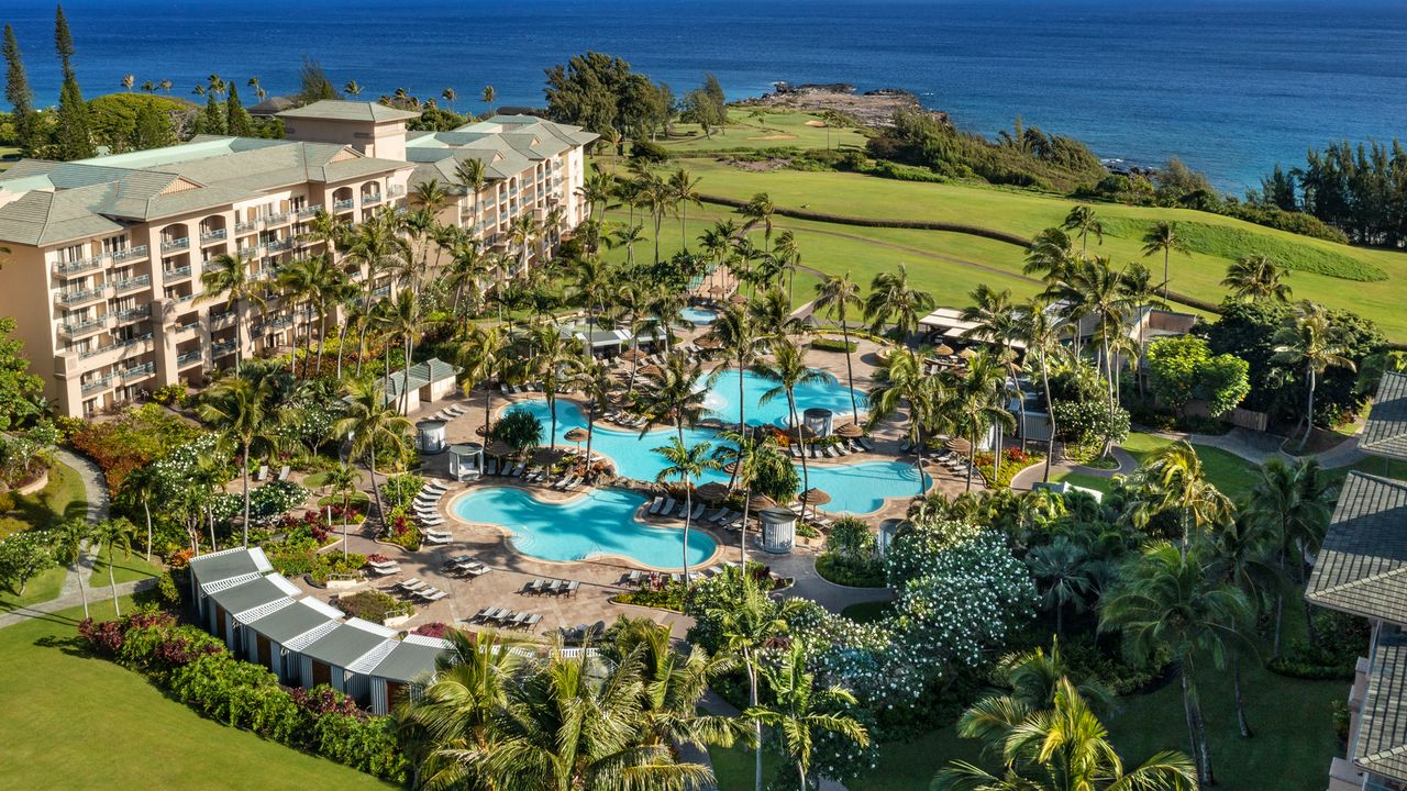 An upscale resort exterior in Wailea featuring expansive pools and palm trees against a clear blue sky.