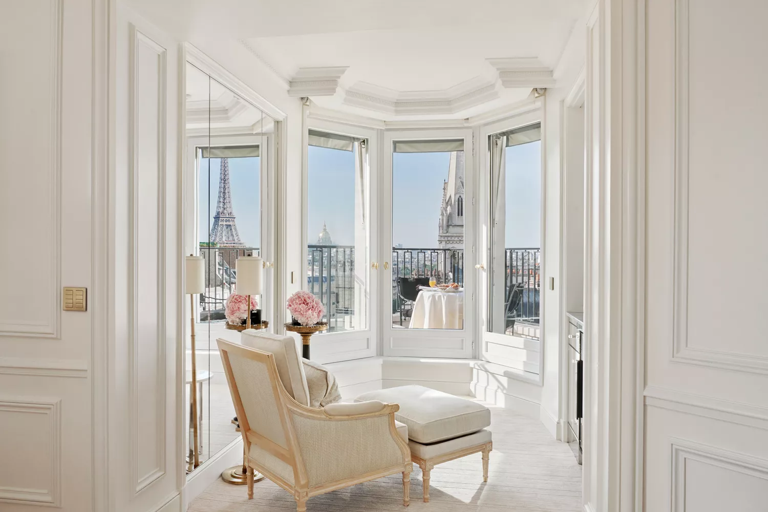 A cozy seating area in a hotel room looking out a window directly at the Eiffel Tower.