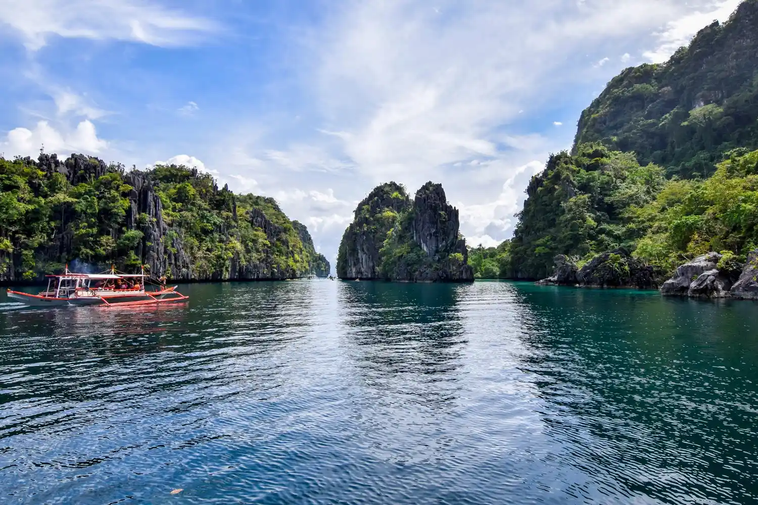 A scenic view featuring rock formations and water in Palawan, Philippines, with a boat on the left side of the frame