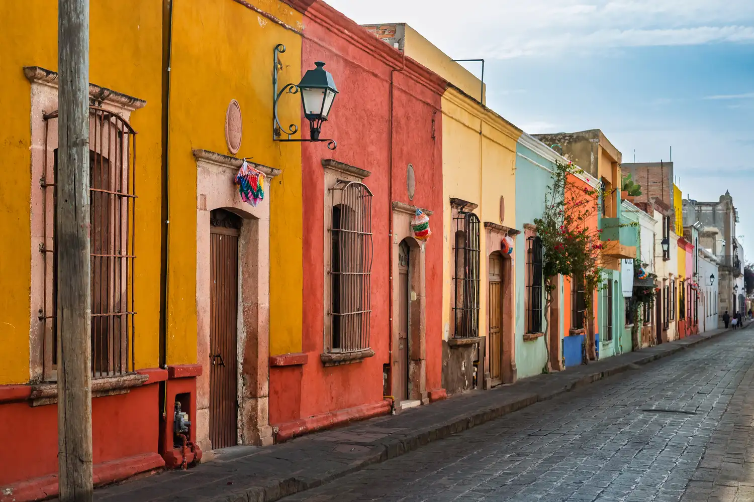 A peaceful cobblestone street in Querétaro flanked by historic colonial-style homes painted in bright orange and yellow.