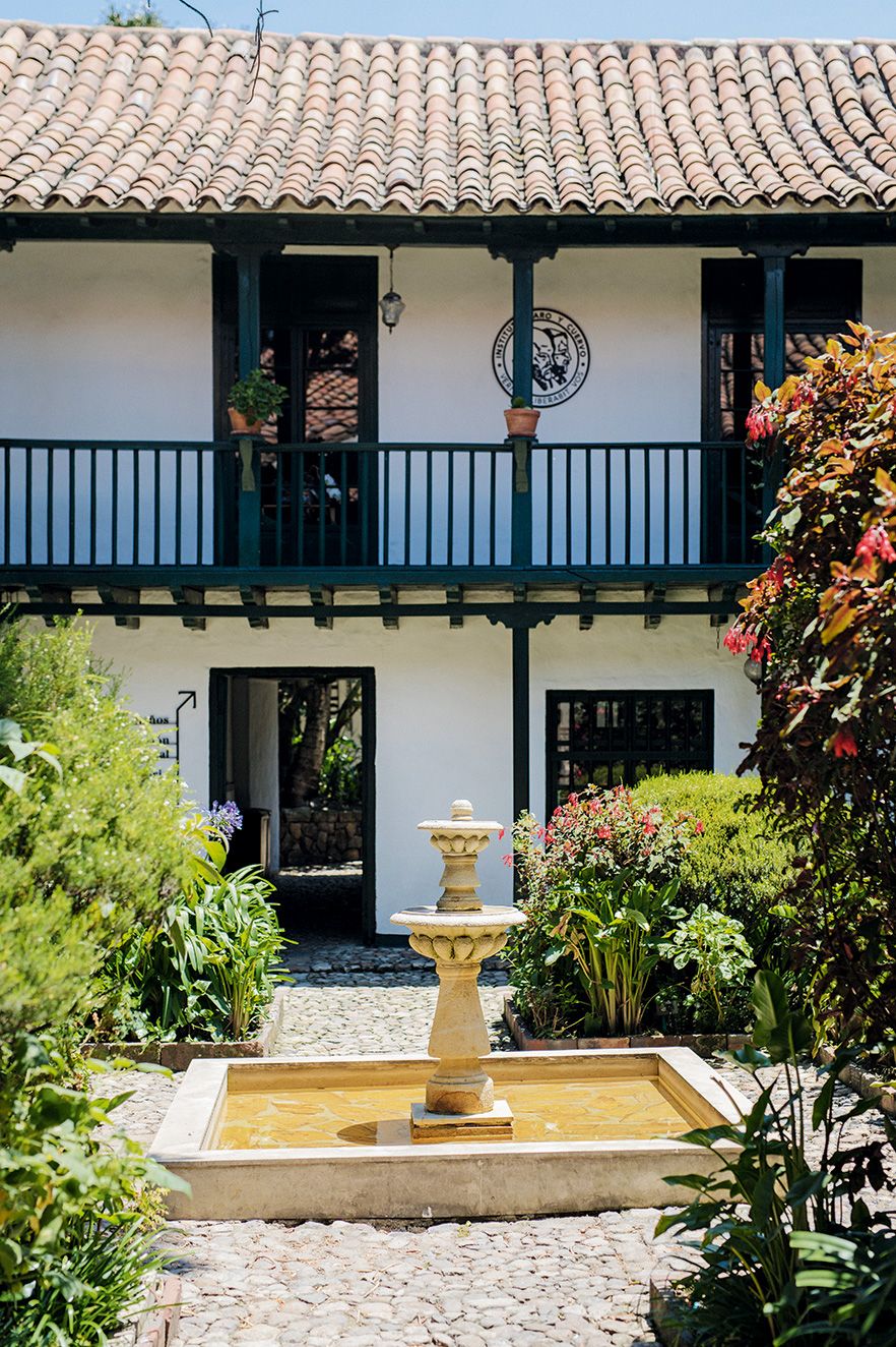 The exterior of a beautifully preserved colonial building in Cartagena surrounded by tropical vegetation.