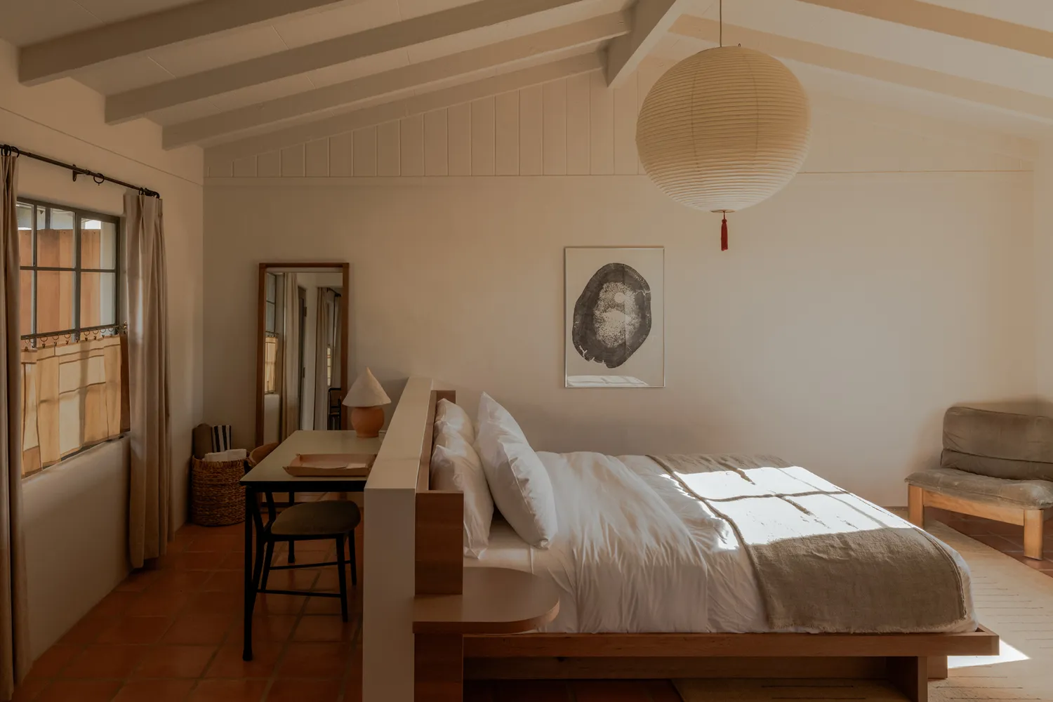 A minimalist hotel room interior with warm lighting, wood accents, and desert-inspired art.