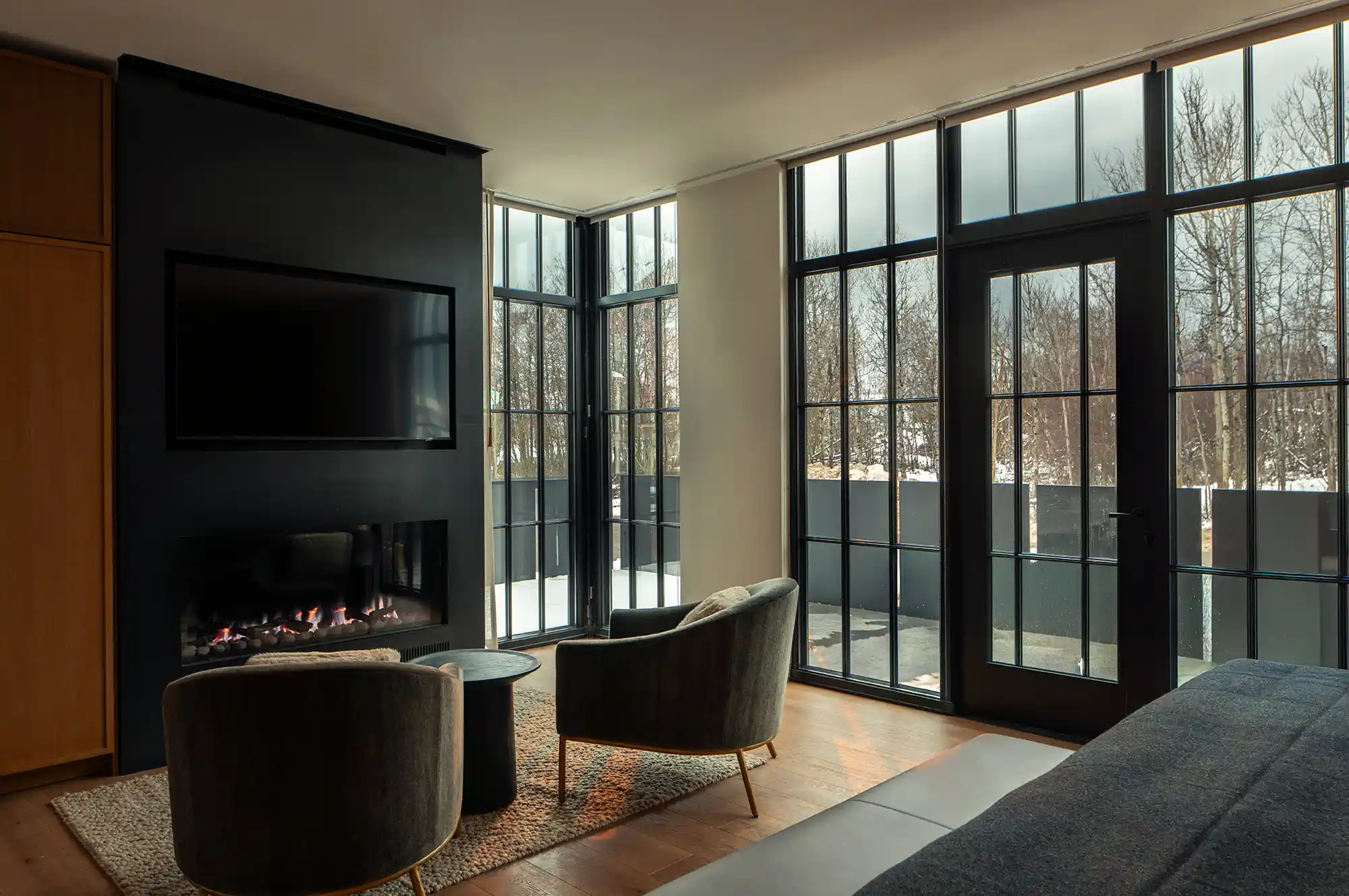 Interior of a modern luxury living room at Larch House with a fireplace and tall windows overlooking the outdoors.