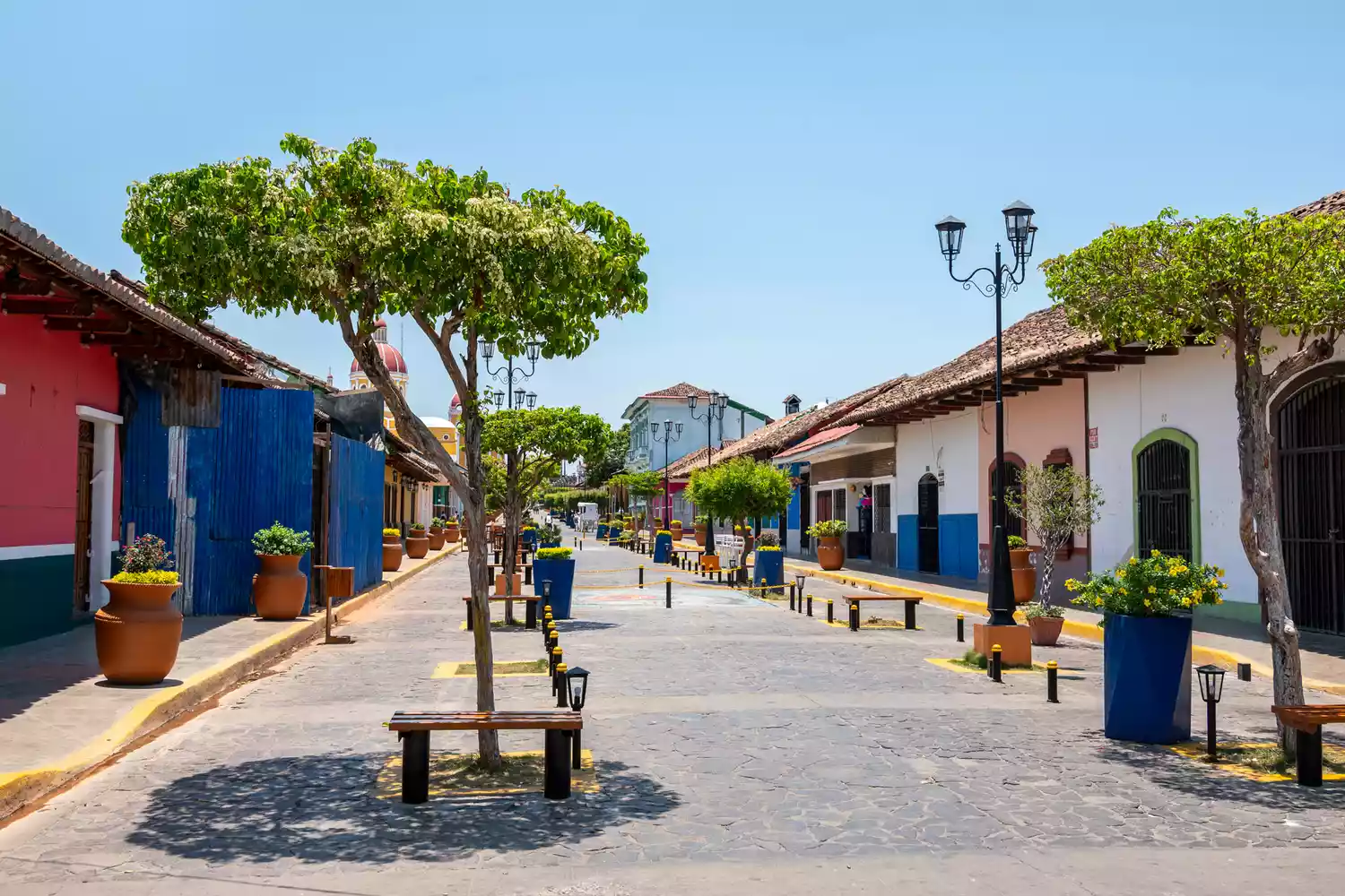 A narrow street in Granada, Nicaragua, lined with bright yellow and red colonial buildings under a blue sky.
