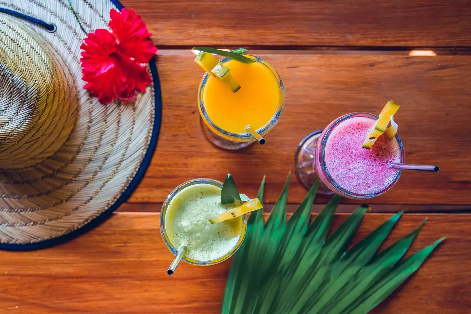 Three vibrant fruit smoothies served on a wooden table in a sunny outdoor setting.