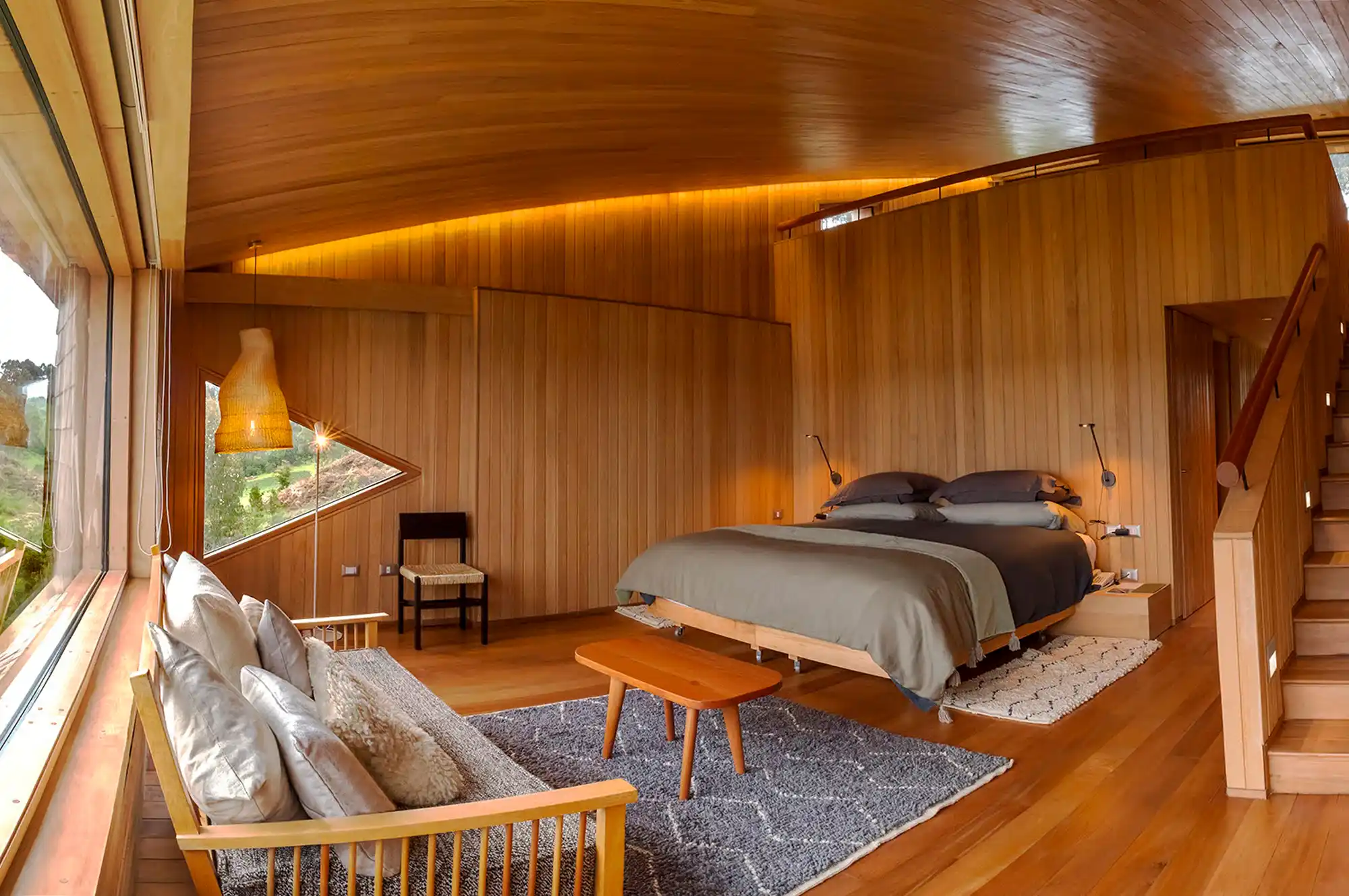 A bright bedroom with wood-paneled walls and a built-in window seat viewing the serene landscape.
