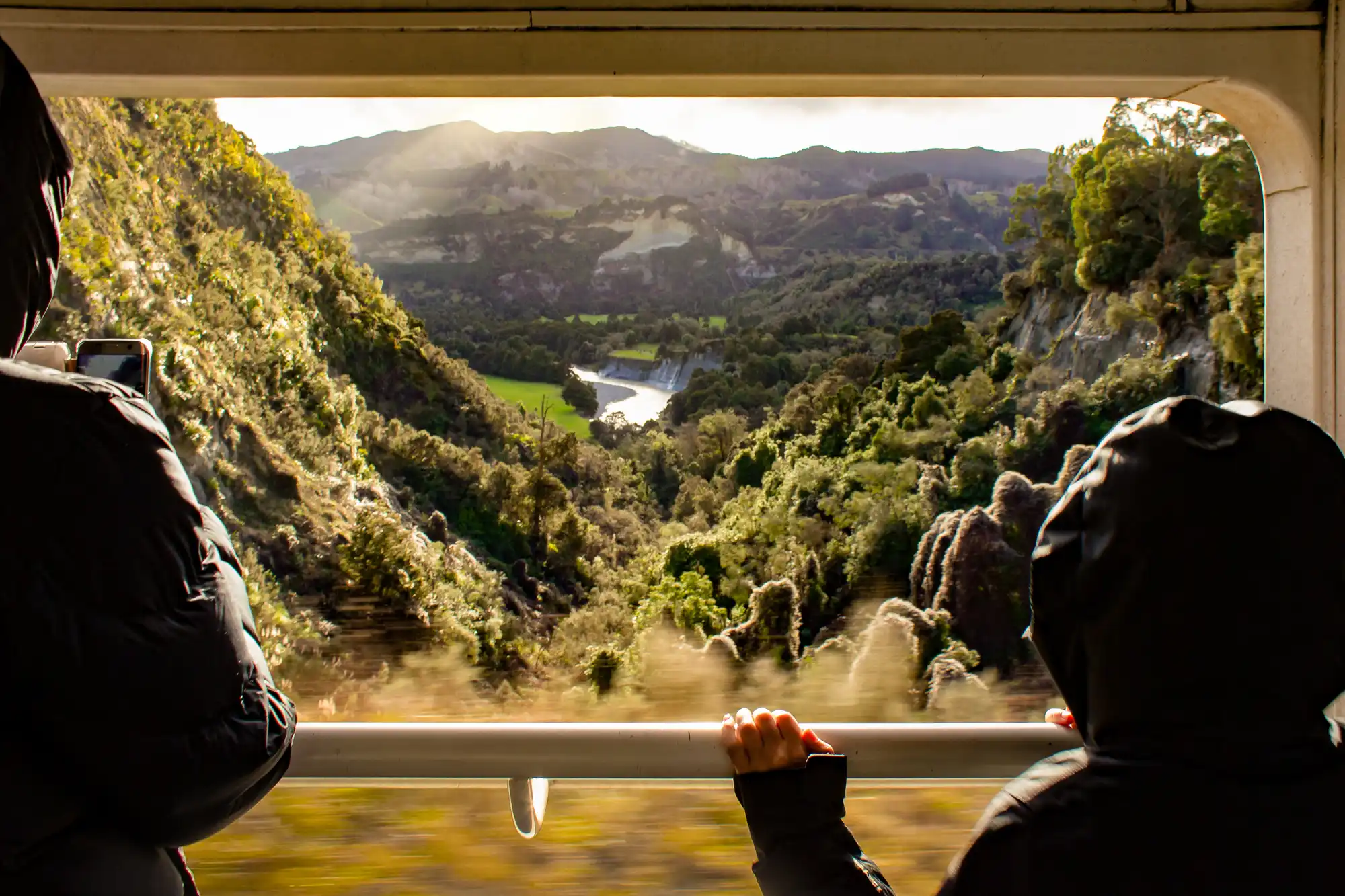 Green hilly landscape and river valley viewed through a large train window.