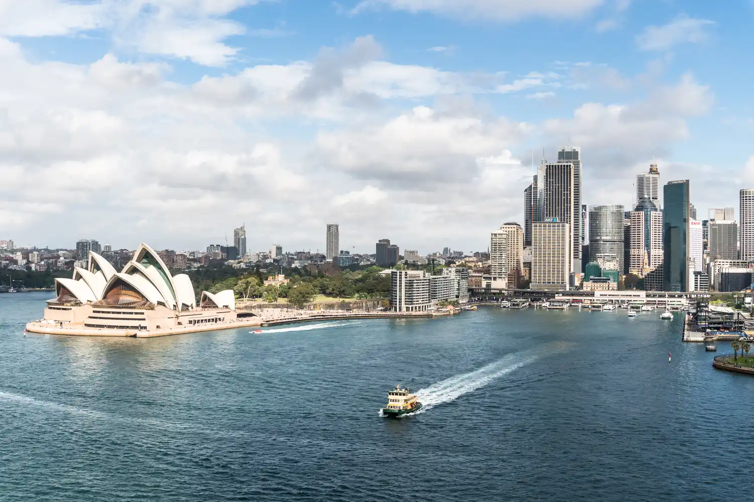 The Sydney Opera House and harbor skyline under a clear blue sky.