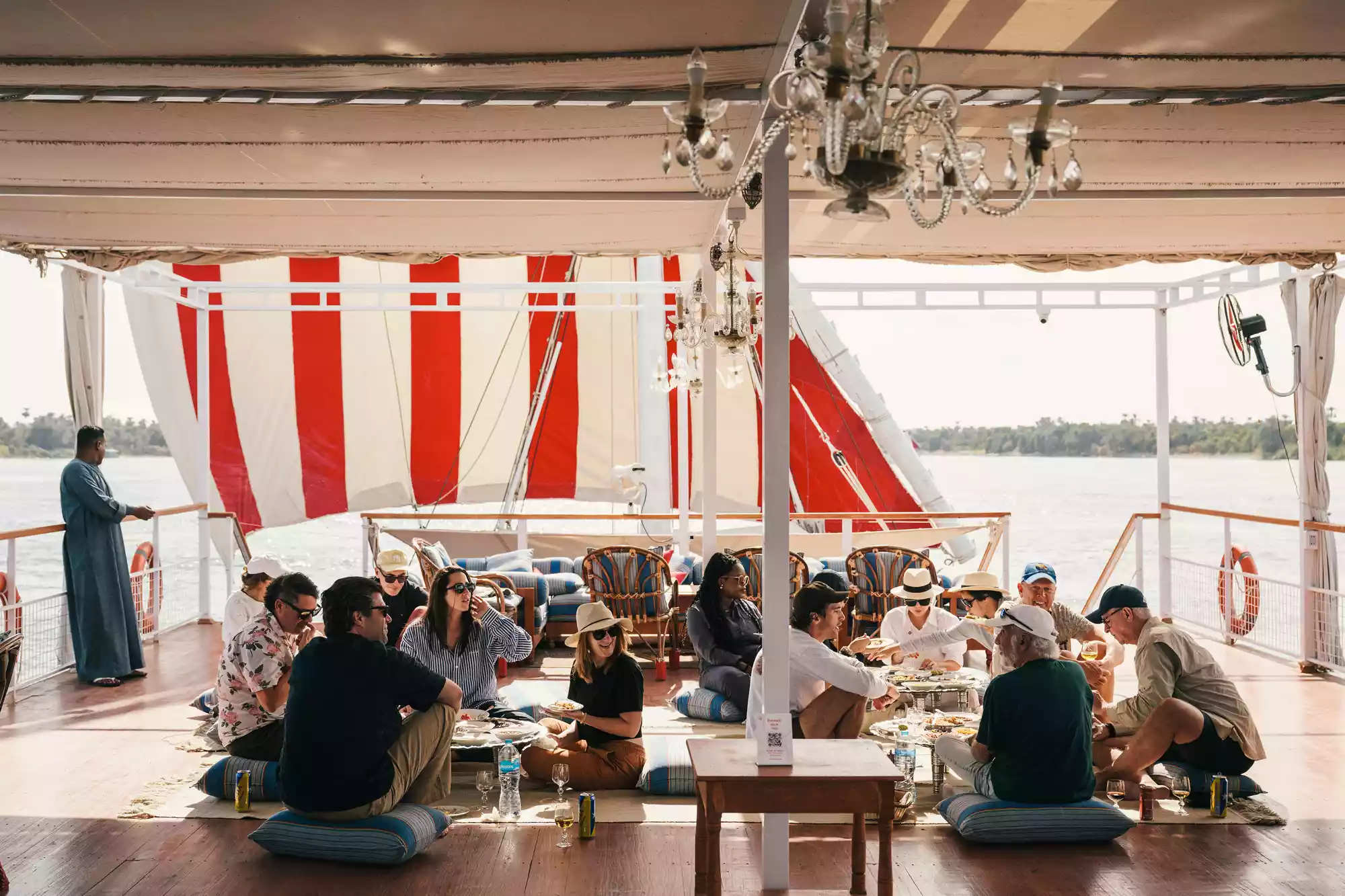 Guests sitting on traditional cushions while dining on the deck of a sailing boat.