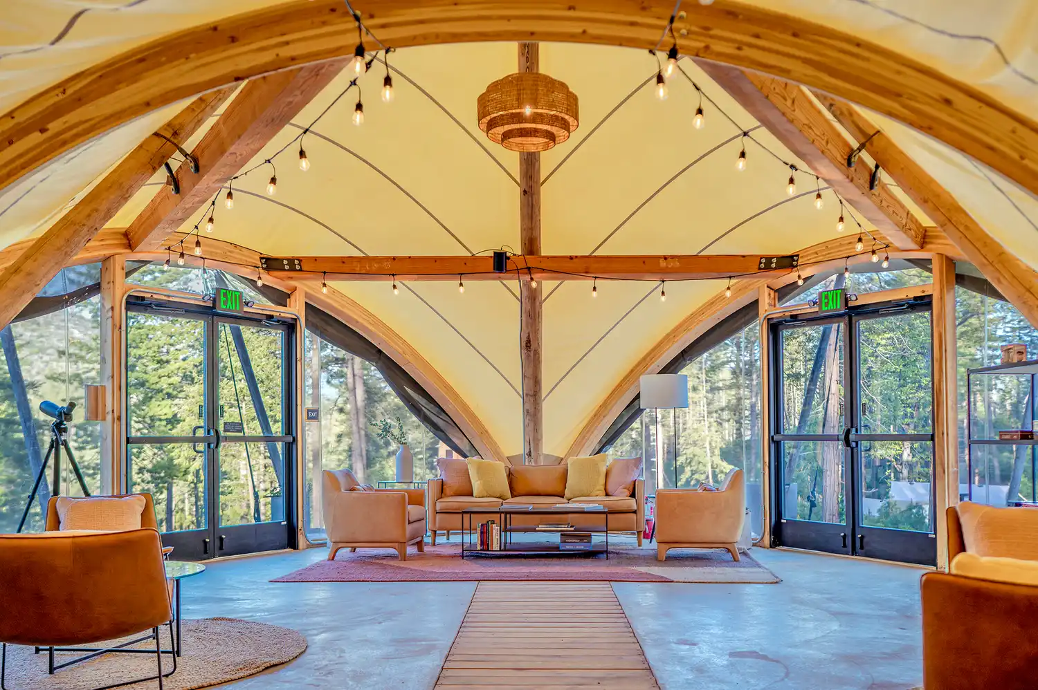 The interior of a large lobby tent with wooden beams, modern rustic chairs, and glass doors.
