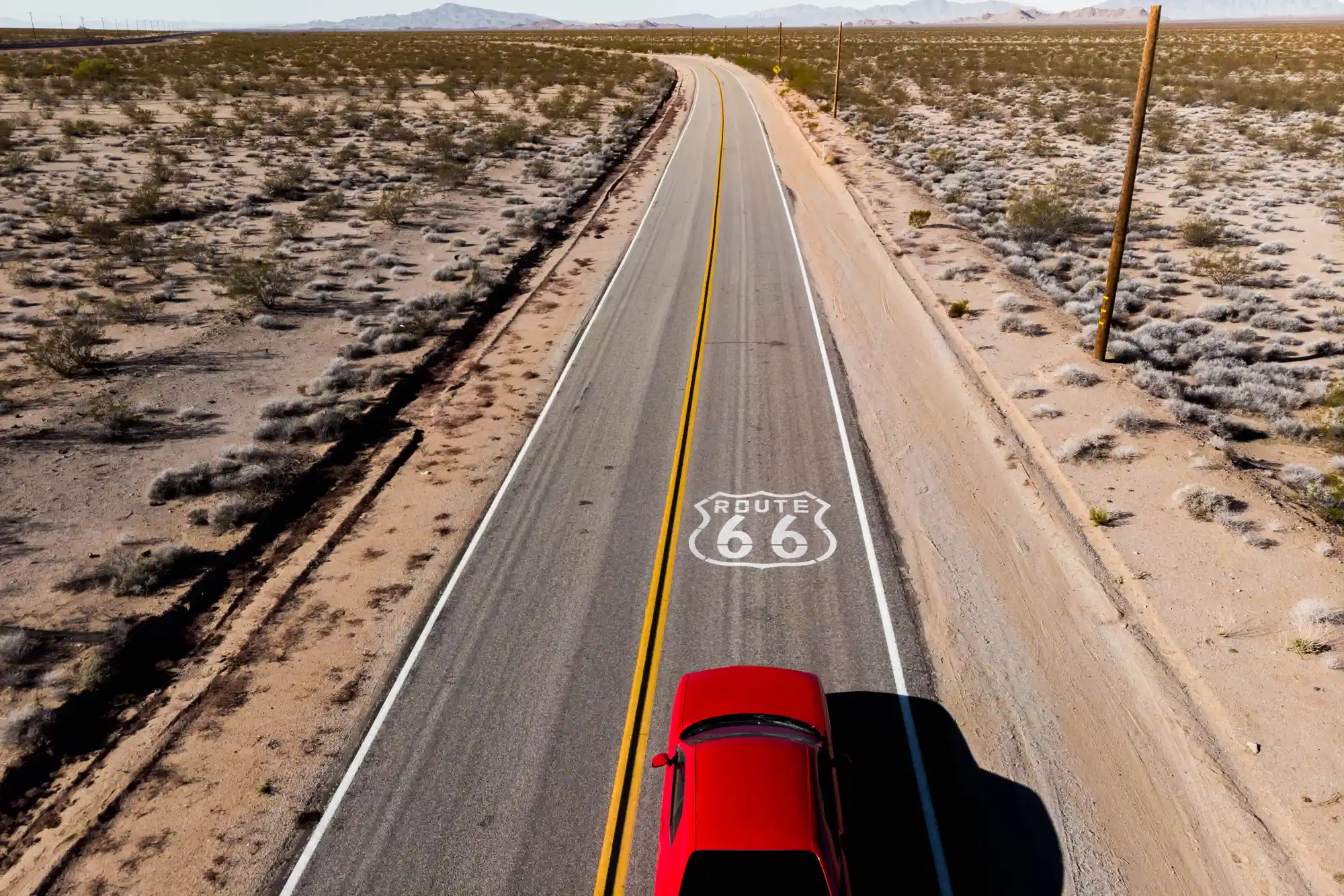 Aerial view of a red car driving on a lonely stretch of historic Route 66 in the desert.
