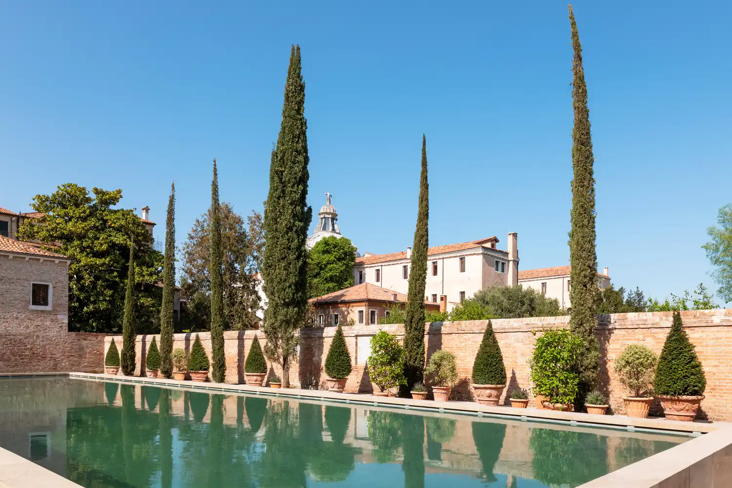 The outdoor swimming pool at Airelles Palladio Venice surrounded by lush greenery and historic architecture.