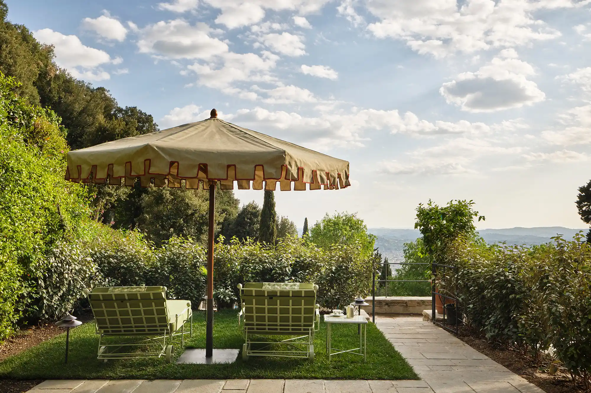 Two lounge chairs under an umbrella overlooking a terraced garden and scenic view.