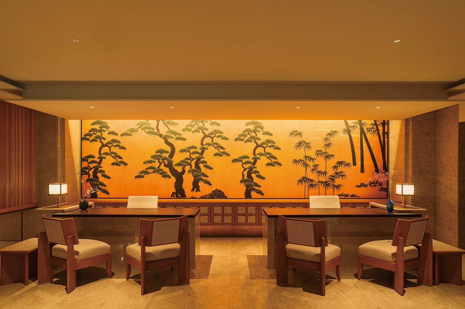 A warm, wood-toned hotel lobby and reception desk with a large tree mural.