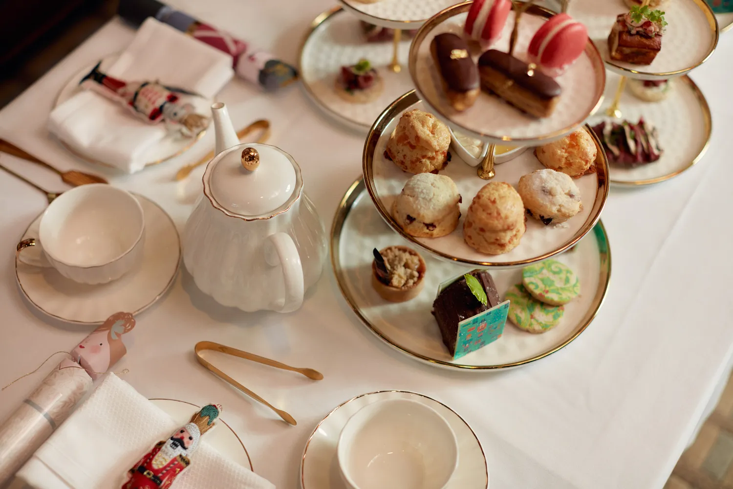 Traditional afternoon tea service with tiered trays of desserts and a white teapot.