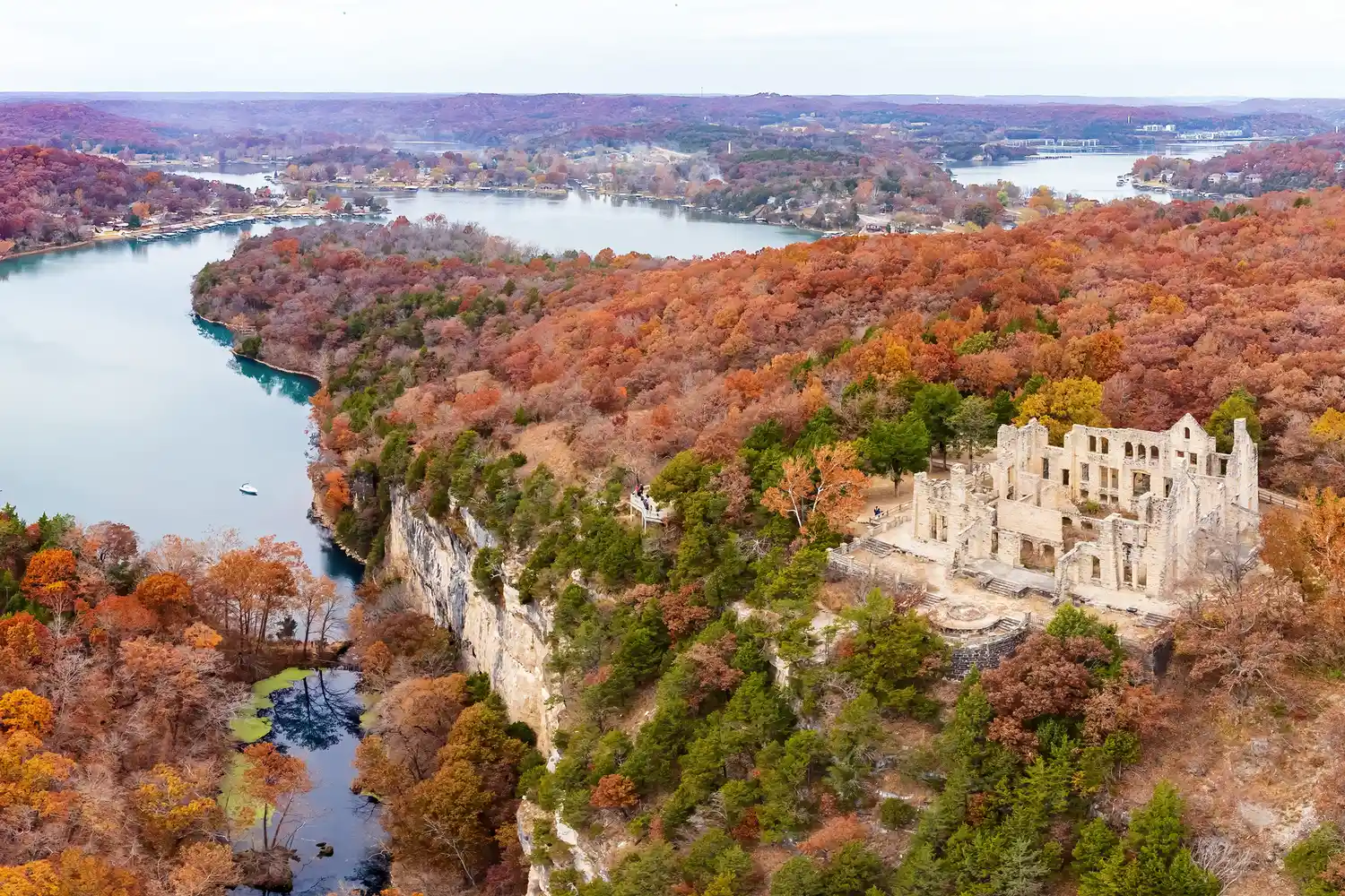 Aerial view of Ha Ha Tonka State Park ruins overlooking the dense forest and blue waters of Lake Ozark during autumn.