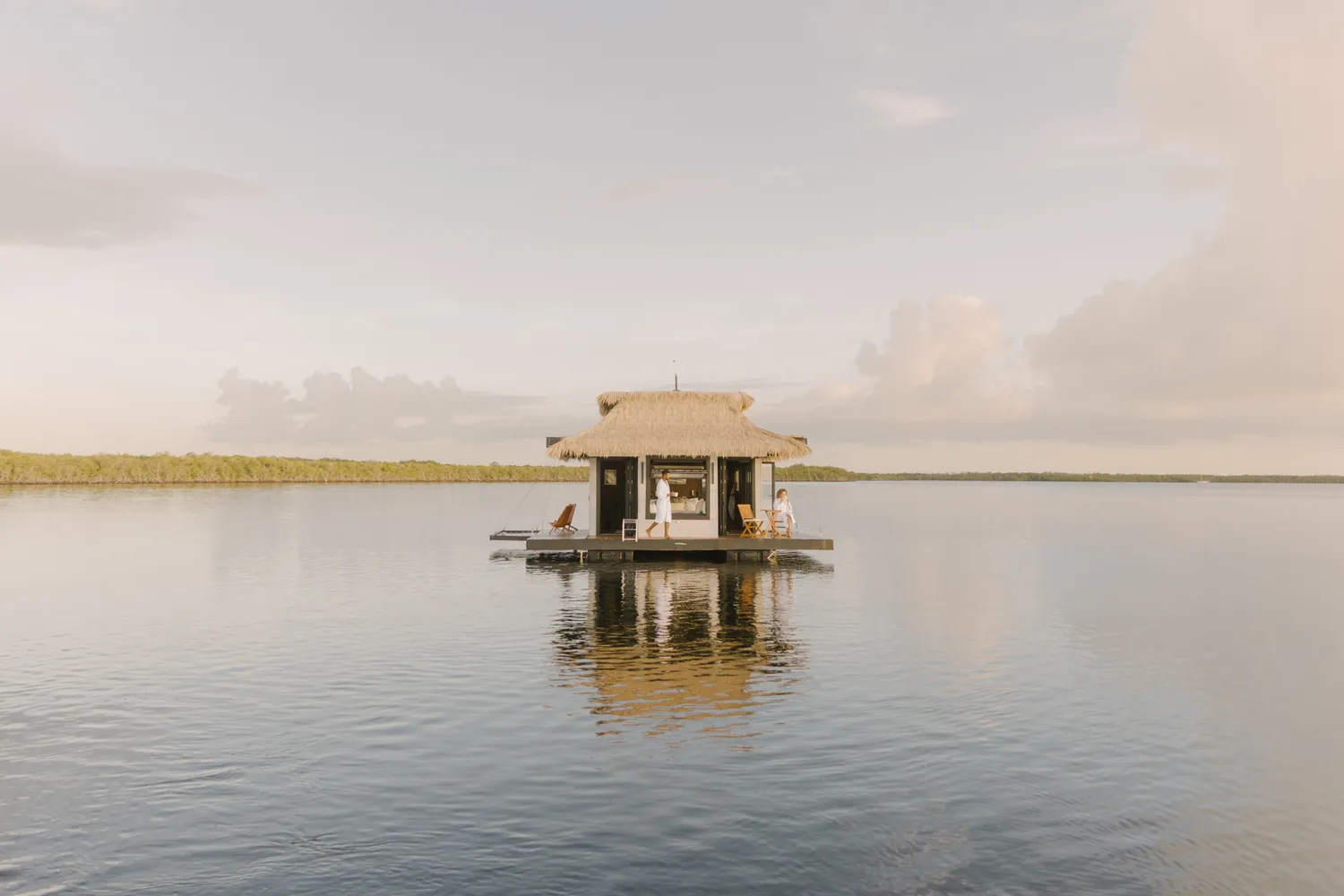 A private floating thatched-roof hut on calm tropical water.