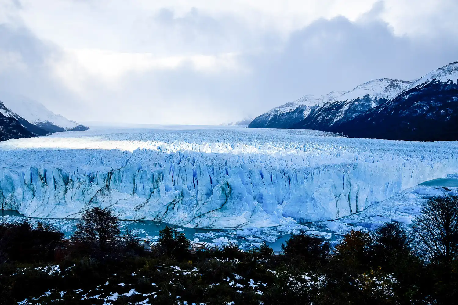 A massive blue-white glacier discharging ice into water between dark mountains.