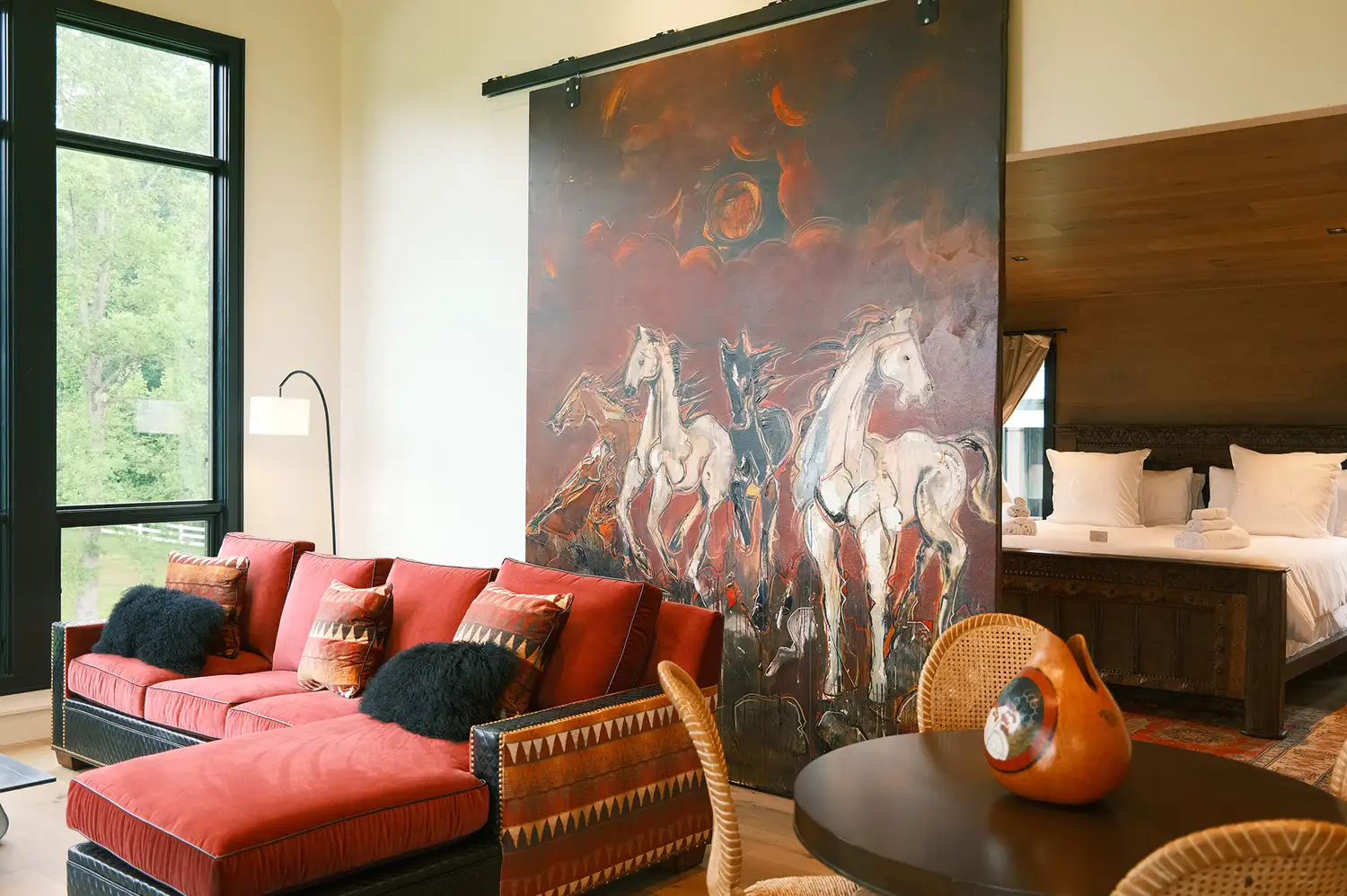 Interior of a Pond Cottage bedroom featuring a red sofa and a large painting of running horses.