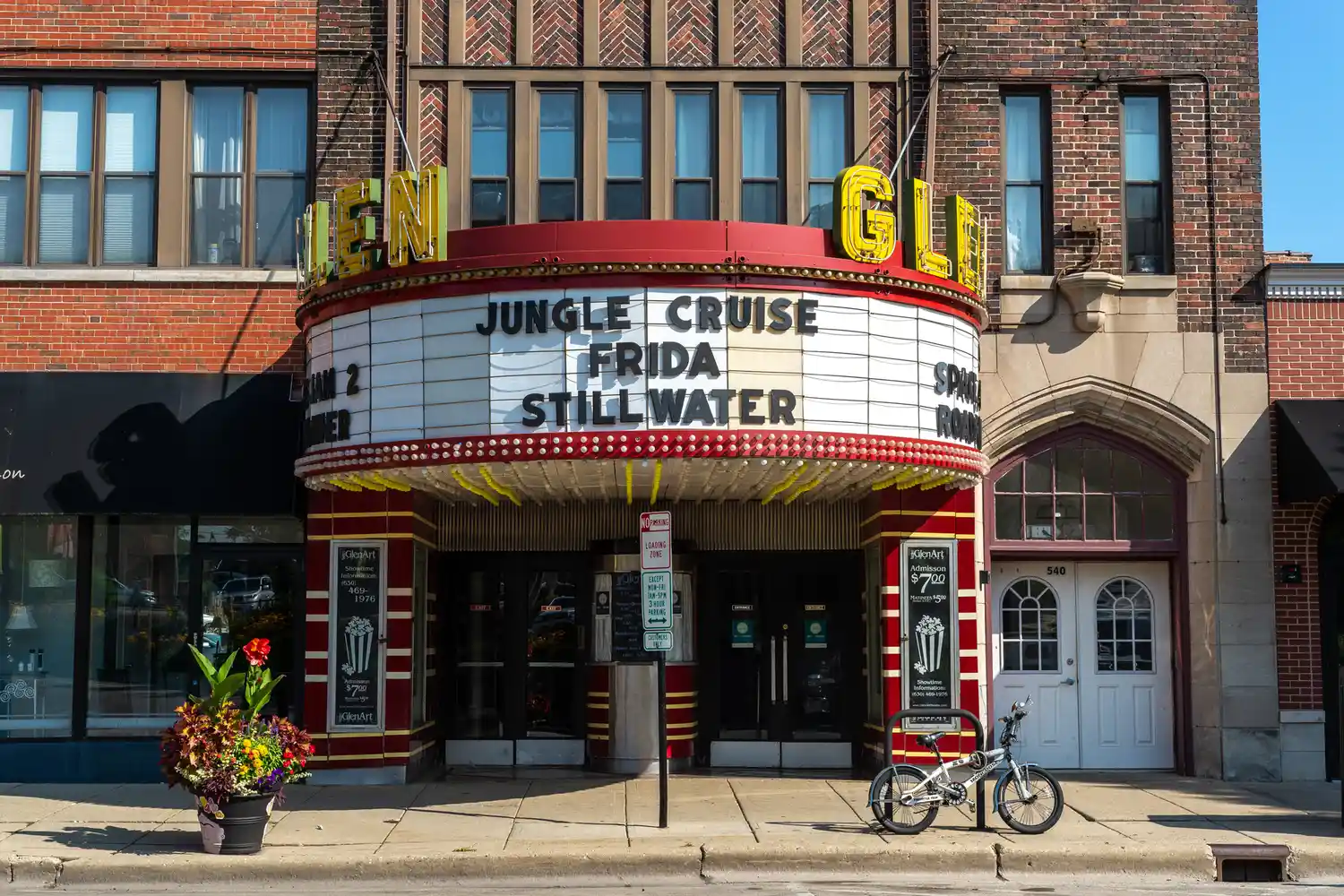 A theater marquee displays movies titles Jungle Cruise Frida and Stillwater with a bicycle parked in front