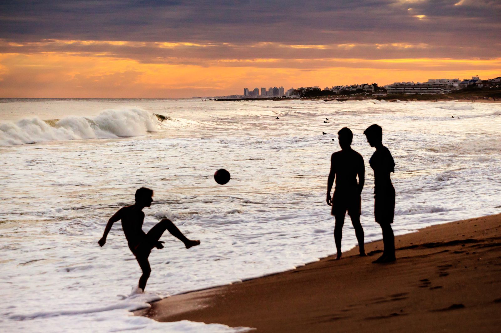 A person playing with a ball on the Montevideo shoreline with the sea in the background.