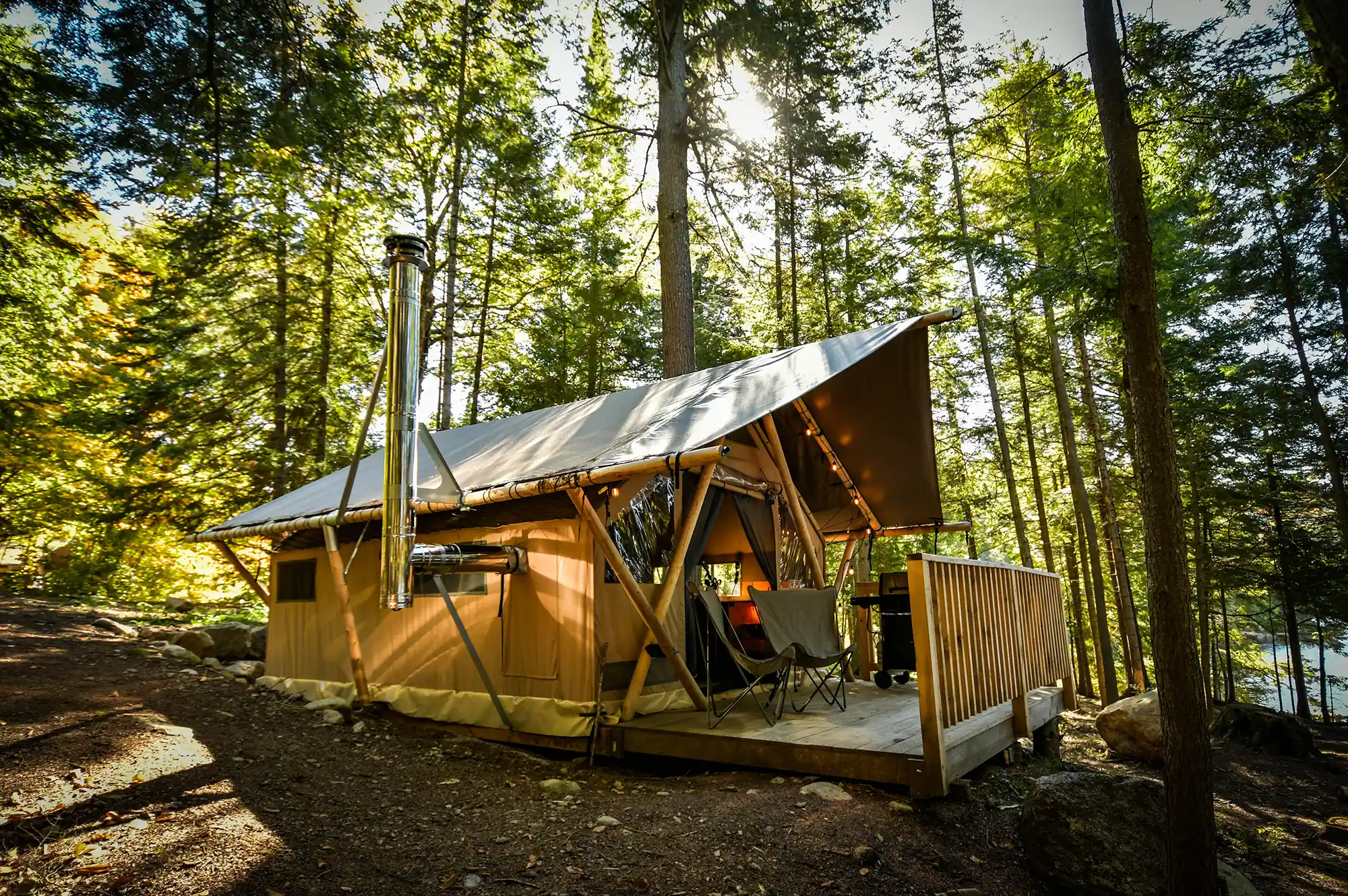 A signature Huttopia wood and canvas tent with a large wooden deck and outdoor chairs in a forest clearing.