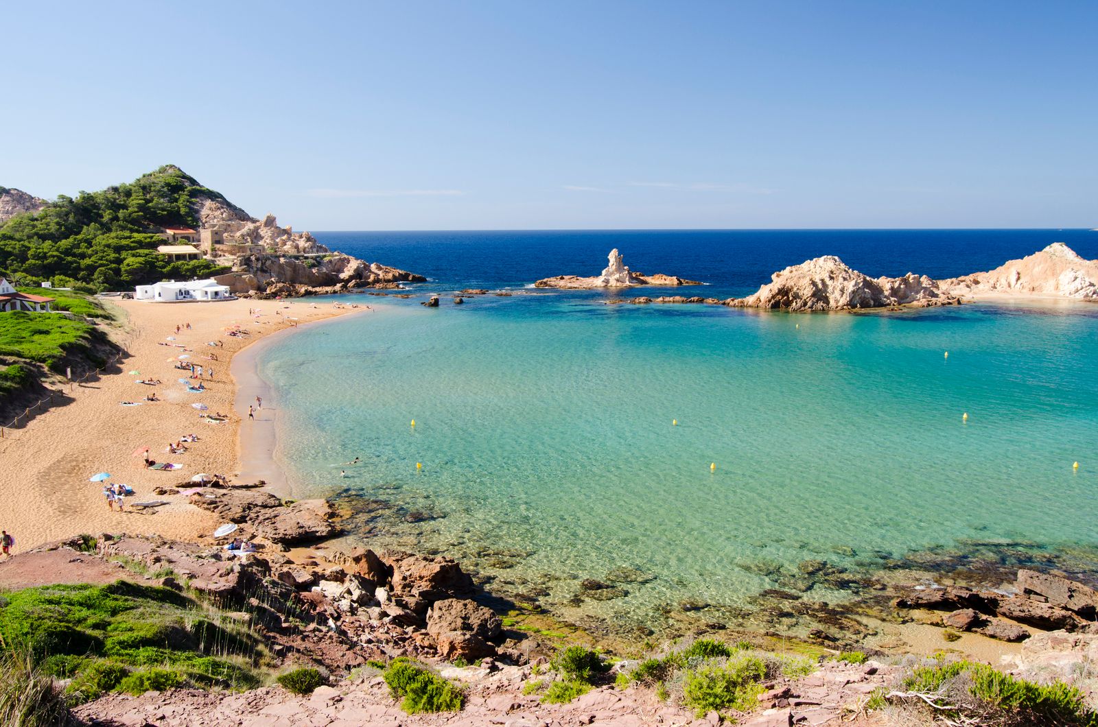 A pristine turquoise lagoon and white sand shoreline under a clear sky.