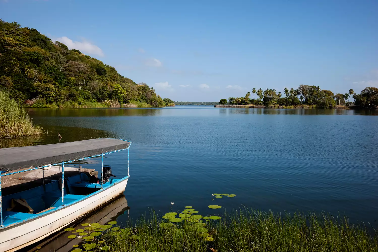 A pontoon boat carrying travelers across the vast, blue waters of Lake Nicaragua under a clear sky.