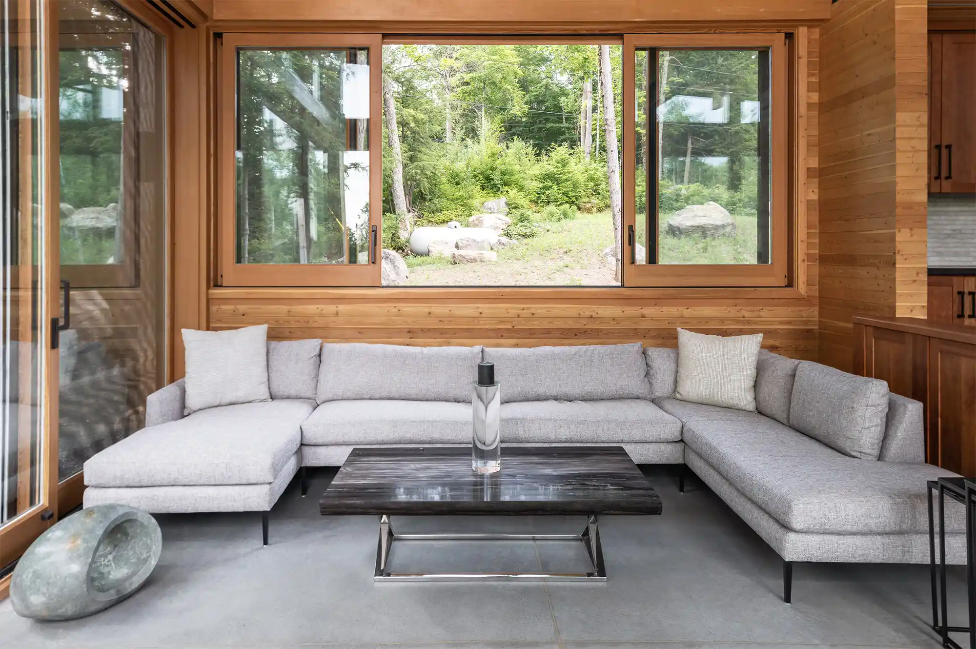 Interior living room of Barlochan Cottage with luxury wooden finishes and floor-to-ceiling windows overlooking a forest.