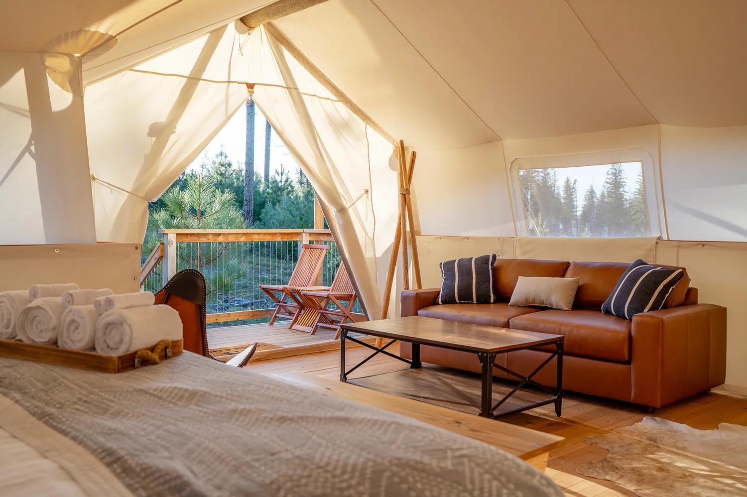 Interior of a glamping tent featuring a leather sofa, wooden floors, and a private deck access.