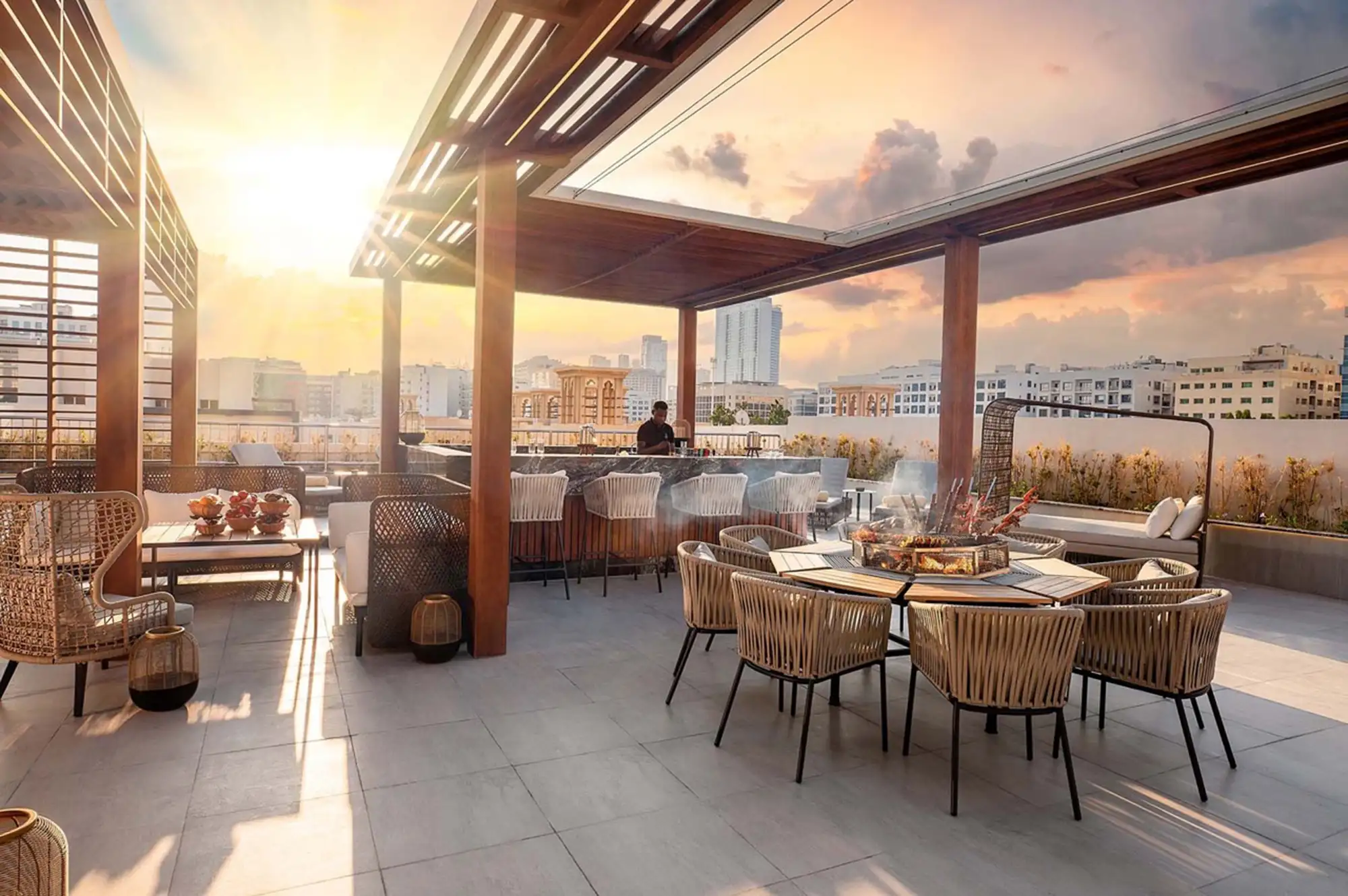A modern rooftop dining and lounge area at sunset with city views.