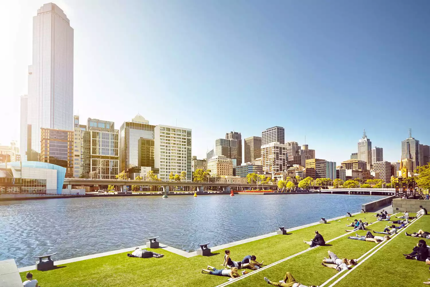 People relaxing by the Yarra River in Melbourne on a sunny day.