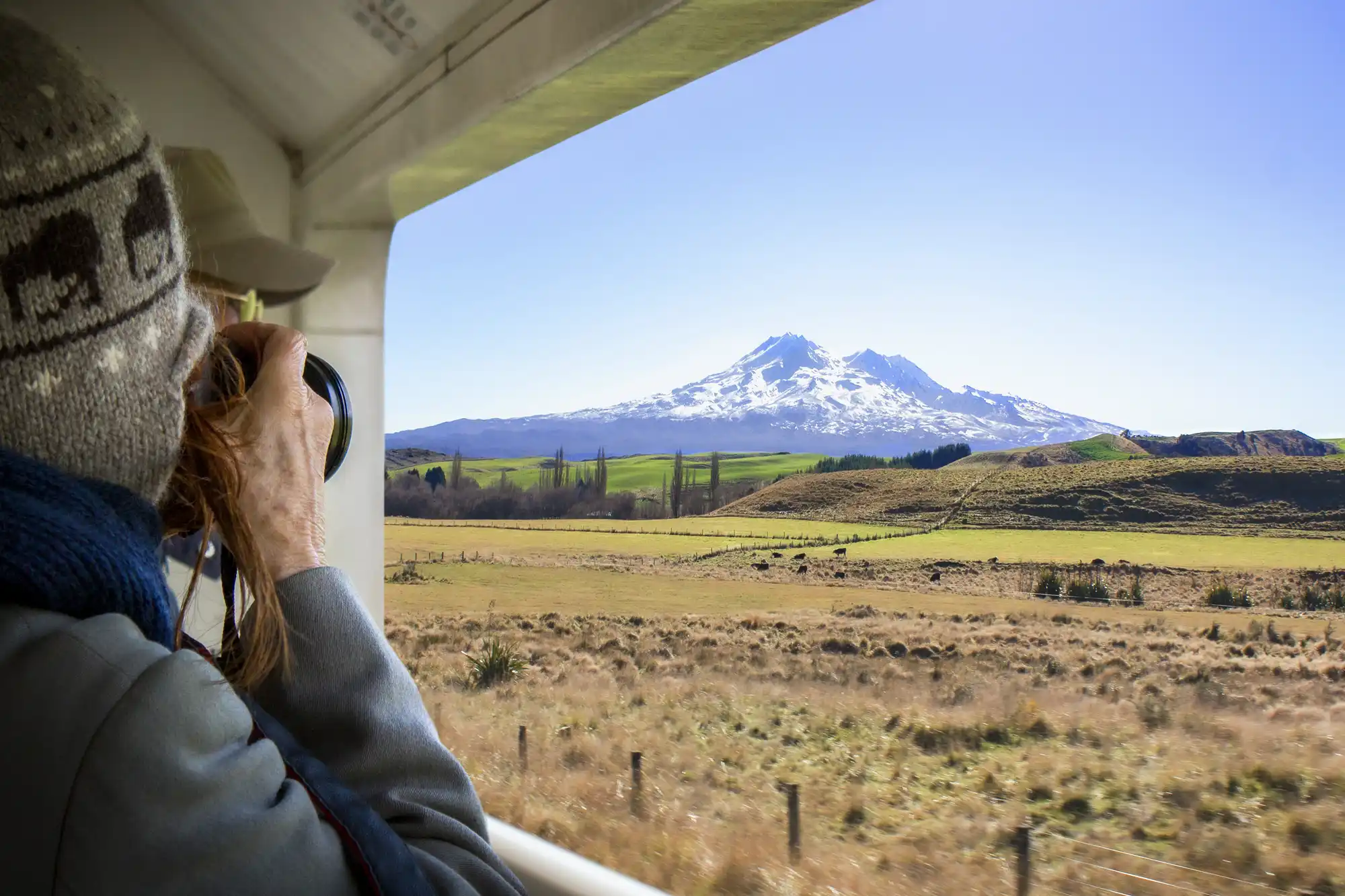 A passenger taking a photo of the snow-capped Mount Ruapehu from inside the train.