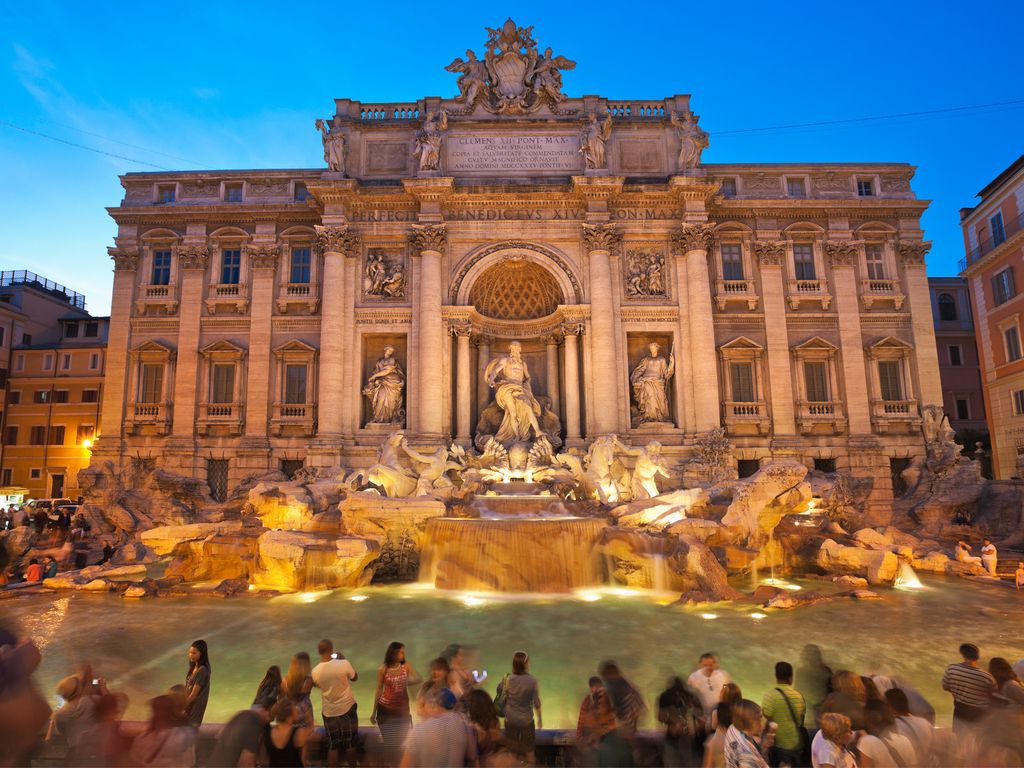 Tourists gathering around the Baroque sculptures of the Trevi Fountain.