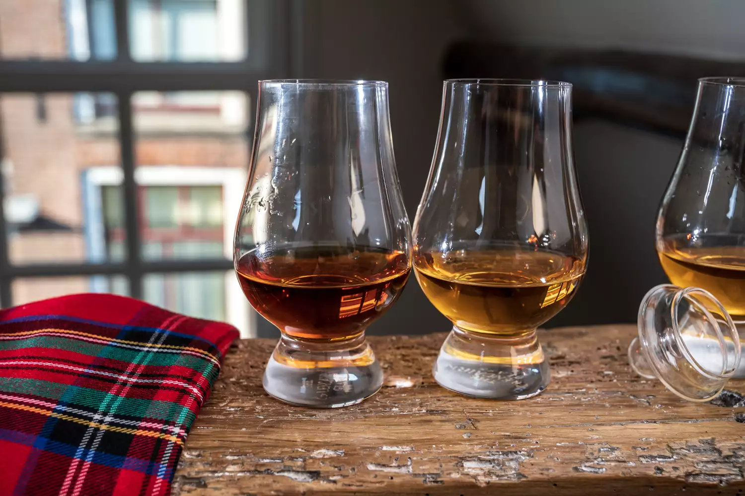 A glass of single malt scotch whisky on a wooden beam with tartan accents.