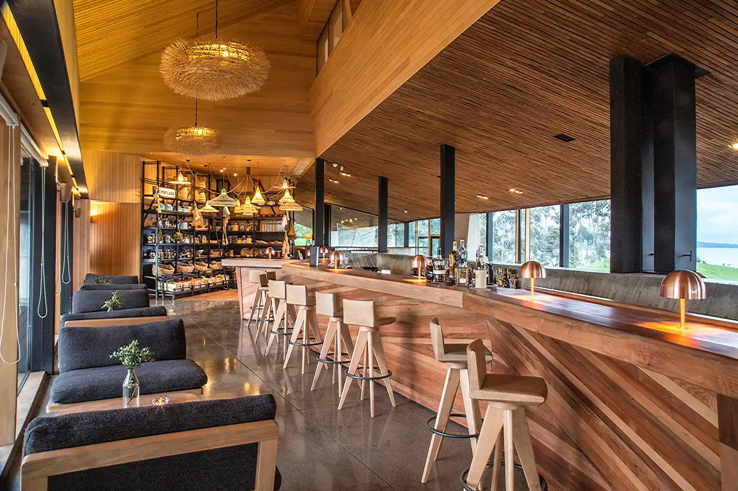 A high-end hotel bar and dining area with wood decor and windows overlooking the green hills of Chiloé.