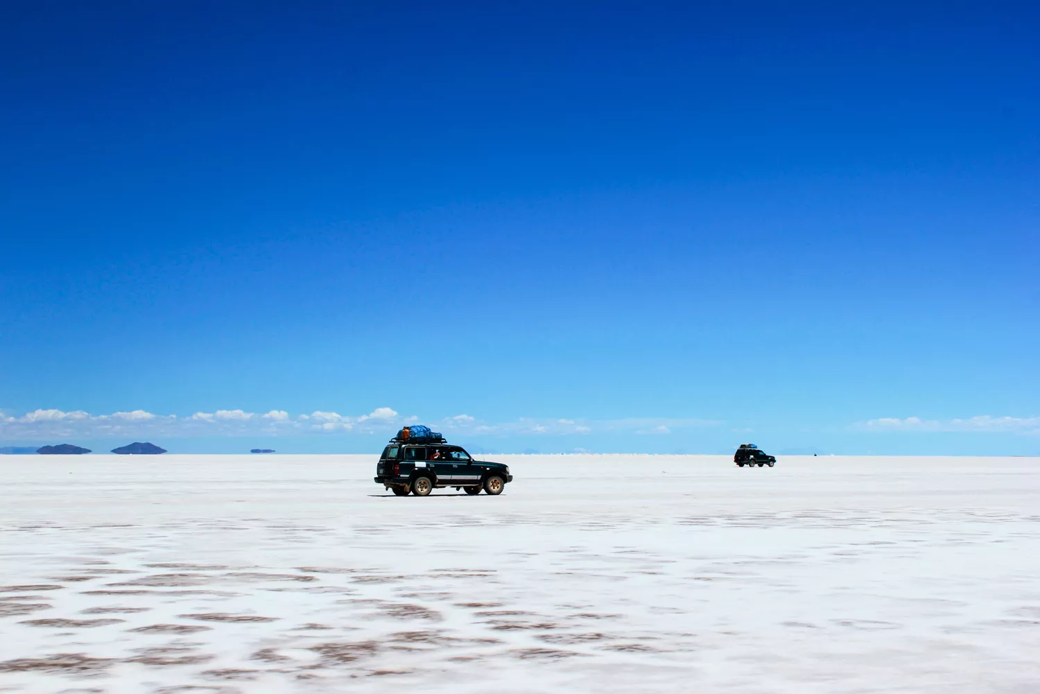 Off-road vehicles driving across the vast, white, reflective surface of the Salar de Uyuni salt flats.