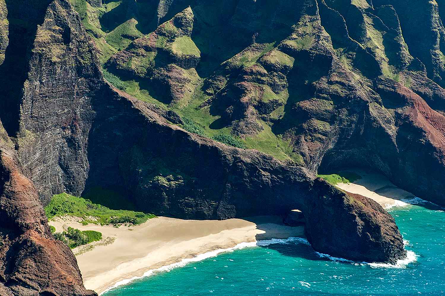 A wide-angle landscape shot of the Honopu Beach Arch and the rugged coastline of Kauai’s Garden Isle.