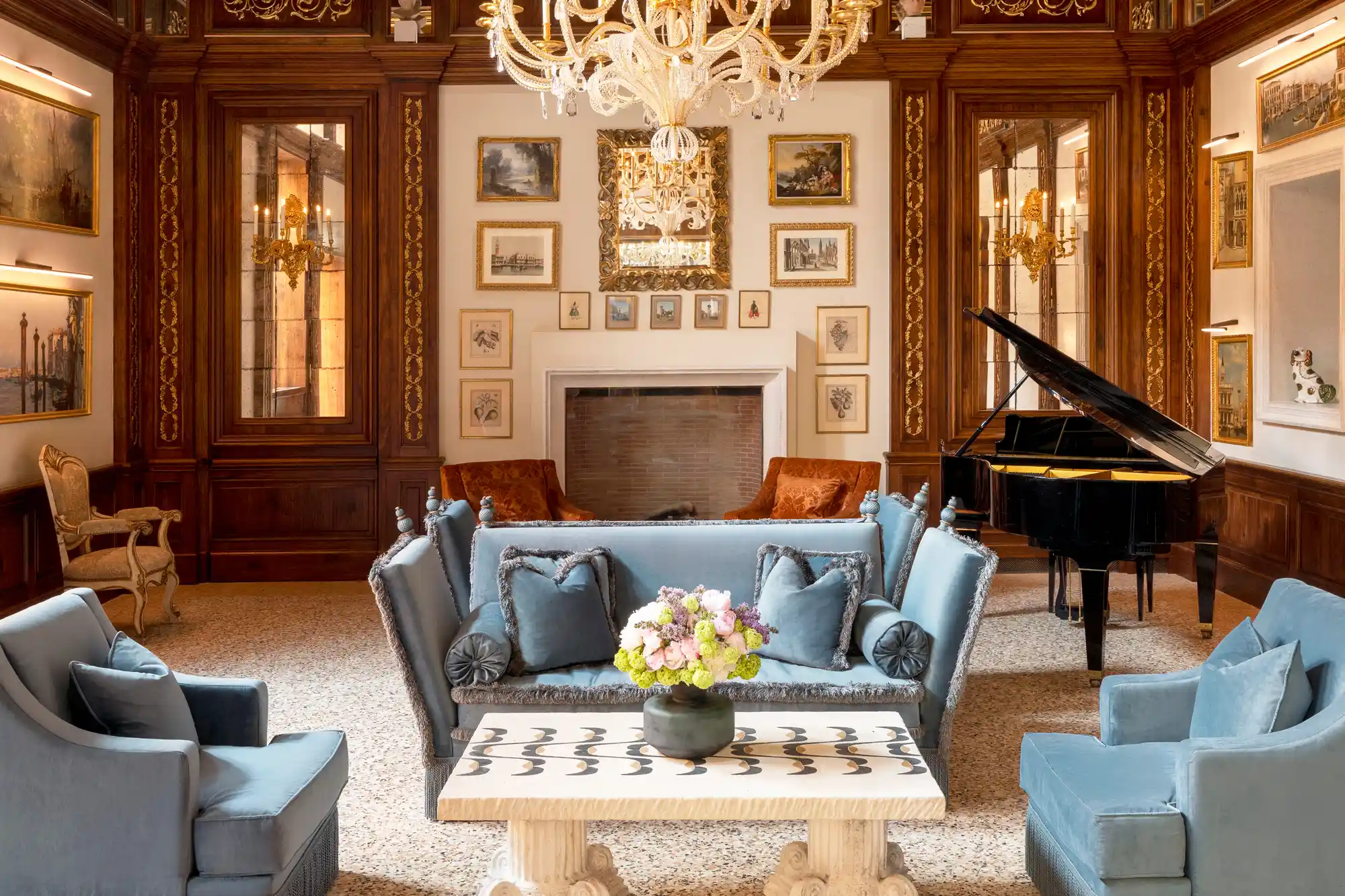 A grand salon in Airelles Palladio with a piano, classical paintings, and a crystal chandelier.