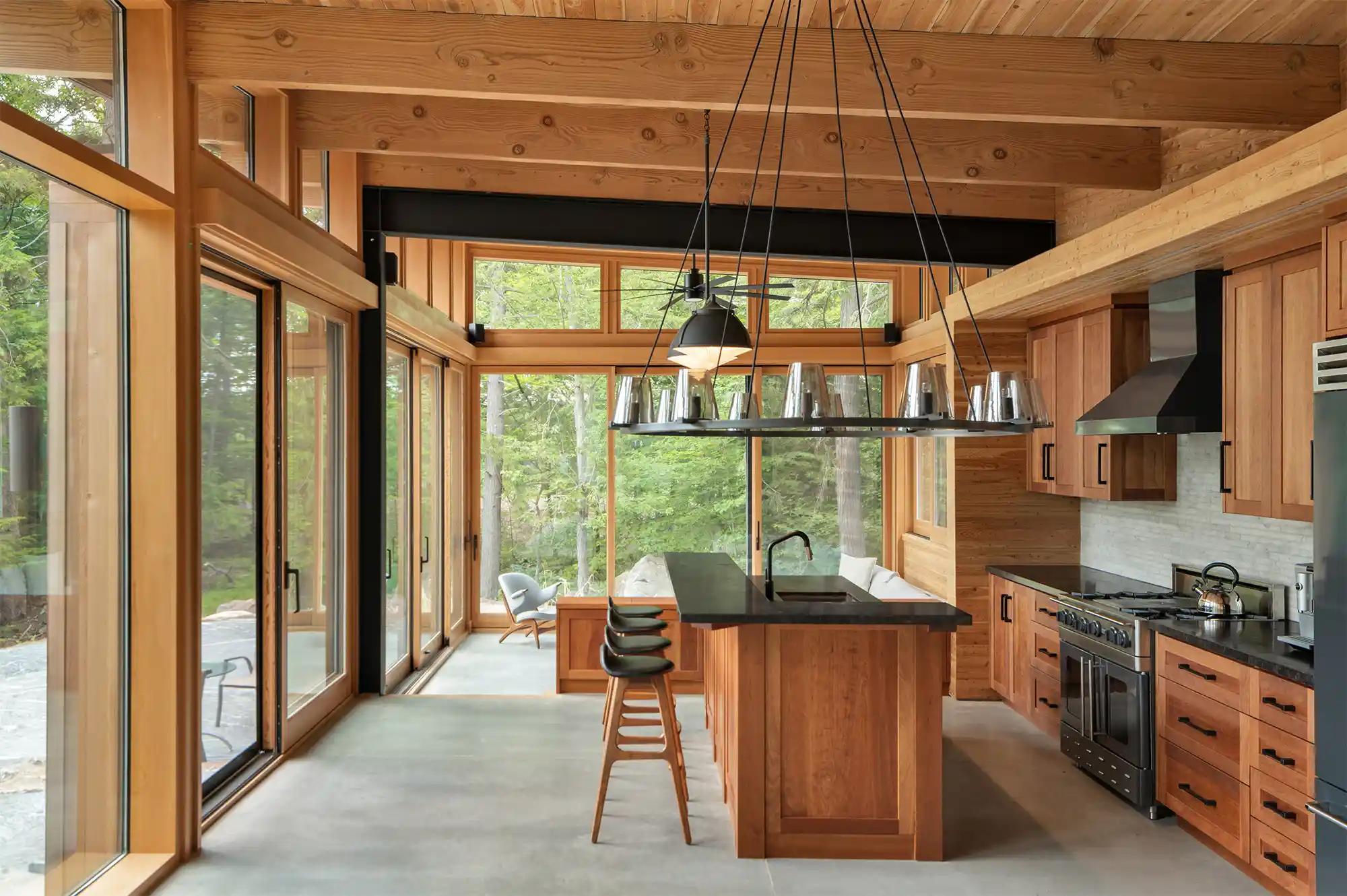 A modern kitchen with a large island and forest views through expansive windows in the Muskoka cottage.