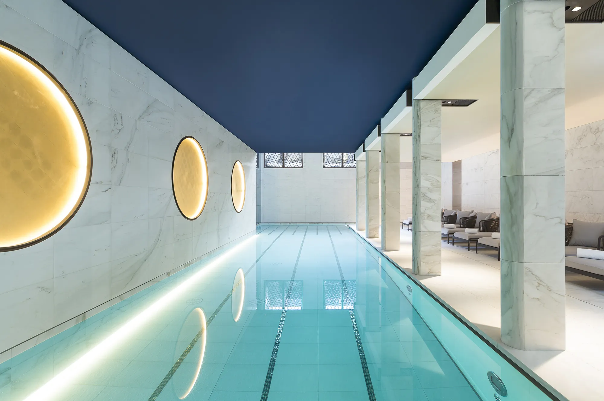 The long indoor swimming pool at Akasha Spa with blue ceiling highlights and marble walls.